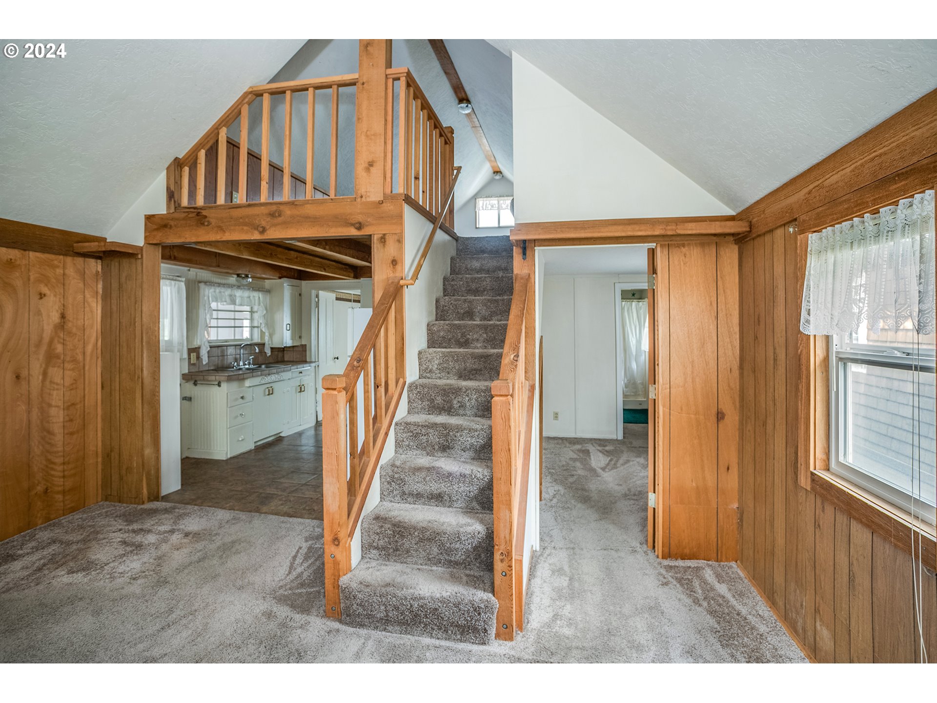 Vacant living area with a carpeted staircase to a loft and wood-paneled walls.