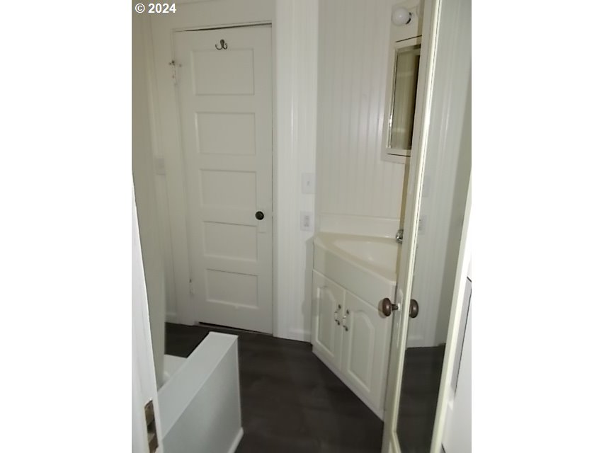 Bathroom with a white vanity and mirror, paneled walls, and the edge of a bathtub.