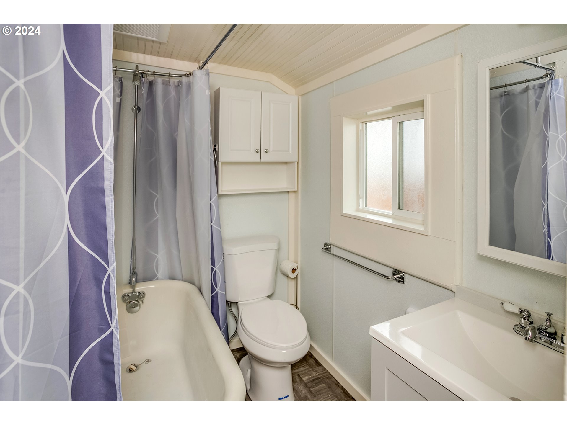Bathroom with a bathtub, purple patterned shower curtain, toilet, and white vanity beneath a wall mirror.