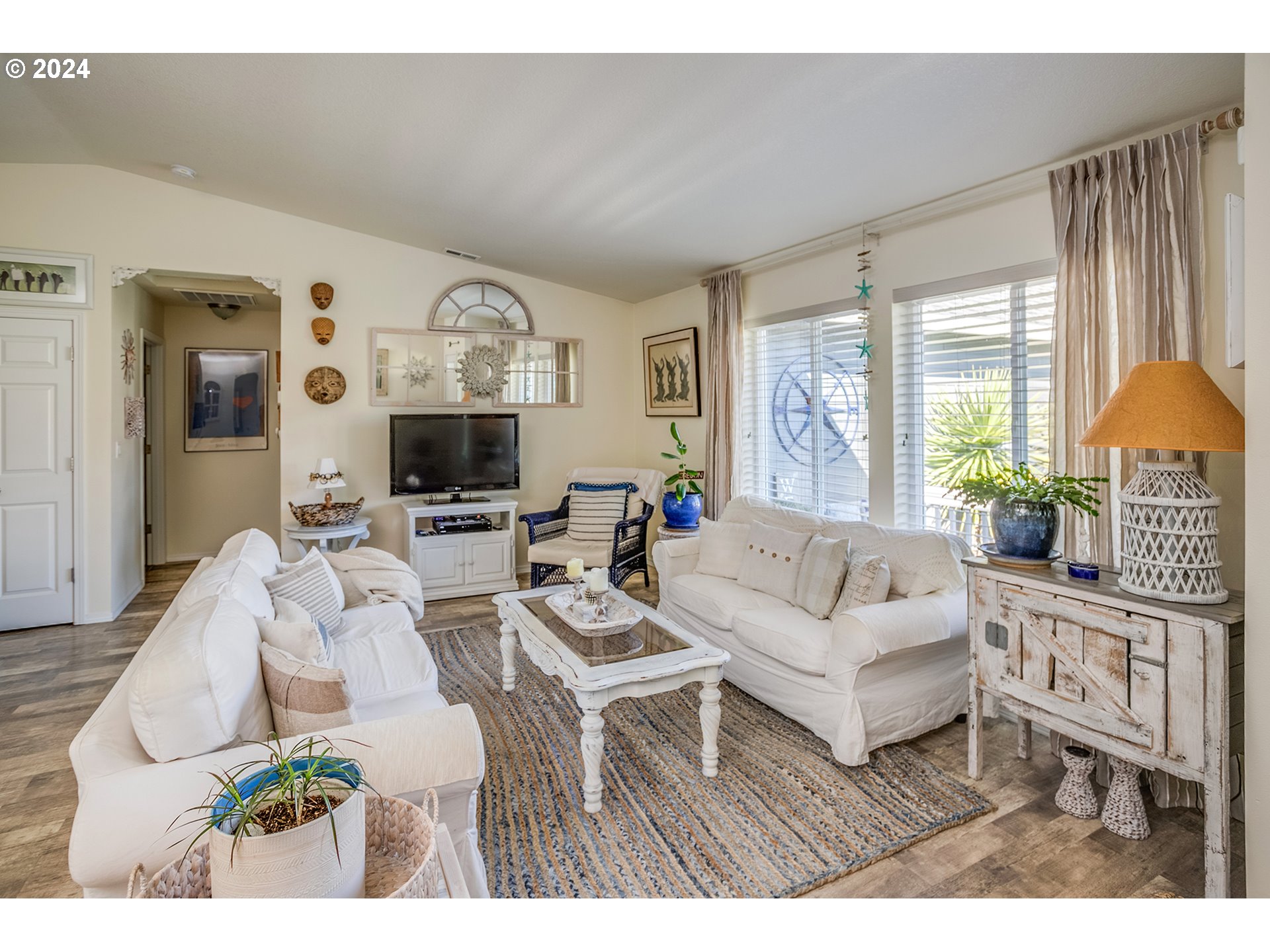 Living room with white sofas, a striped rug, and large curtained windows.