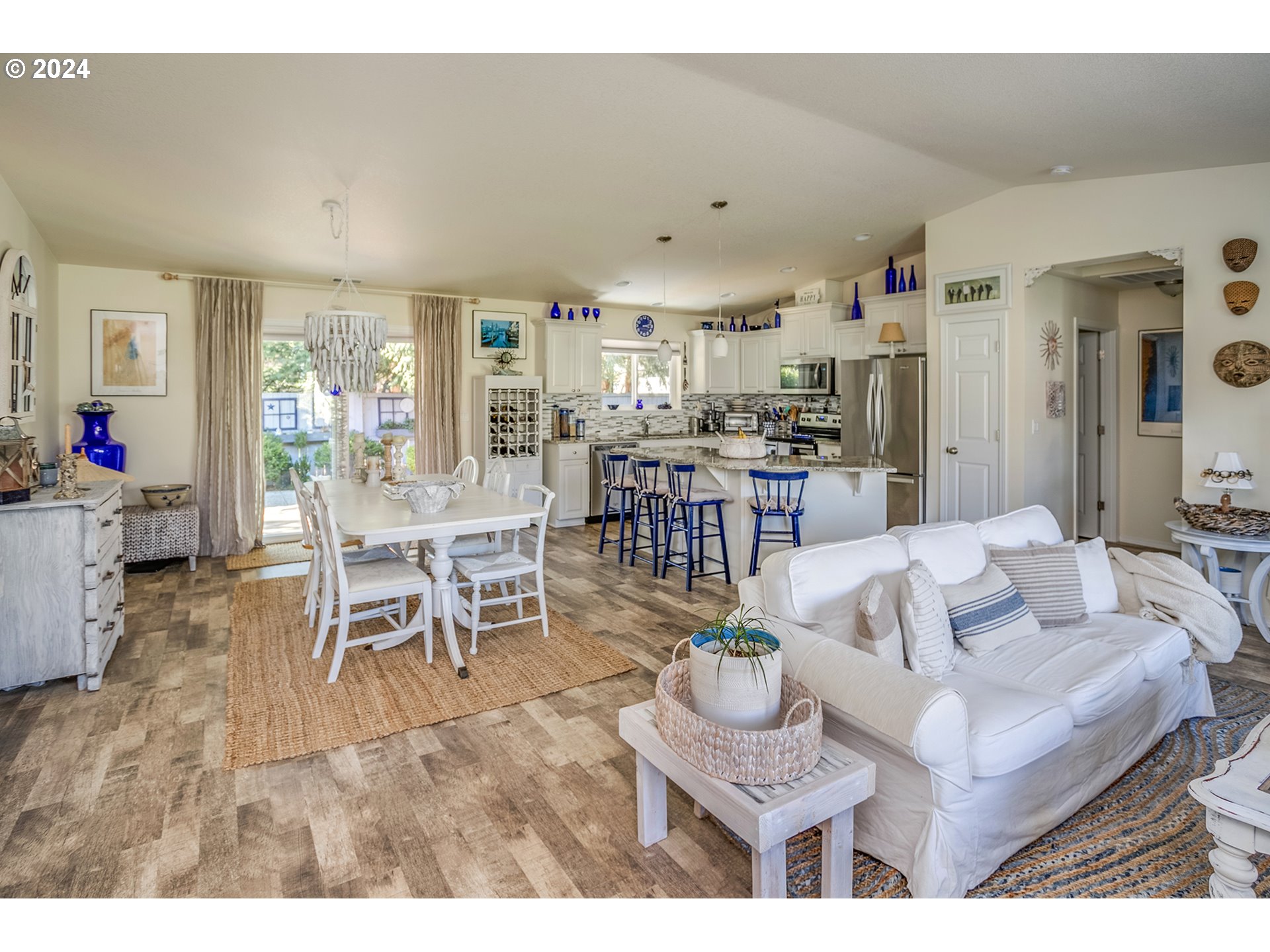 Open-plan living, dining, and kitchen area with a granite island, blue stools, and white furnishings.