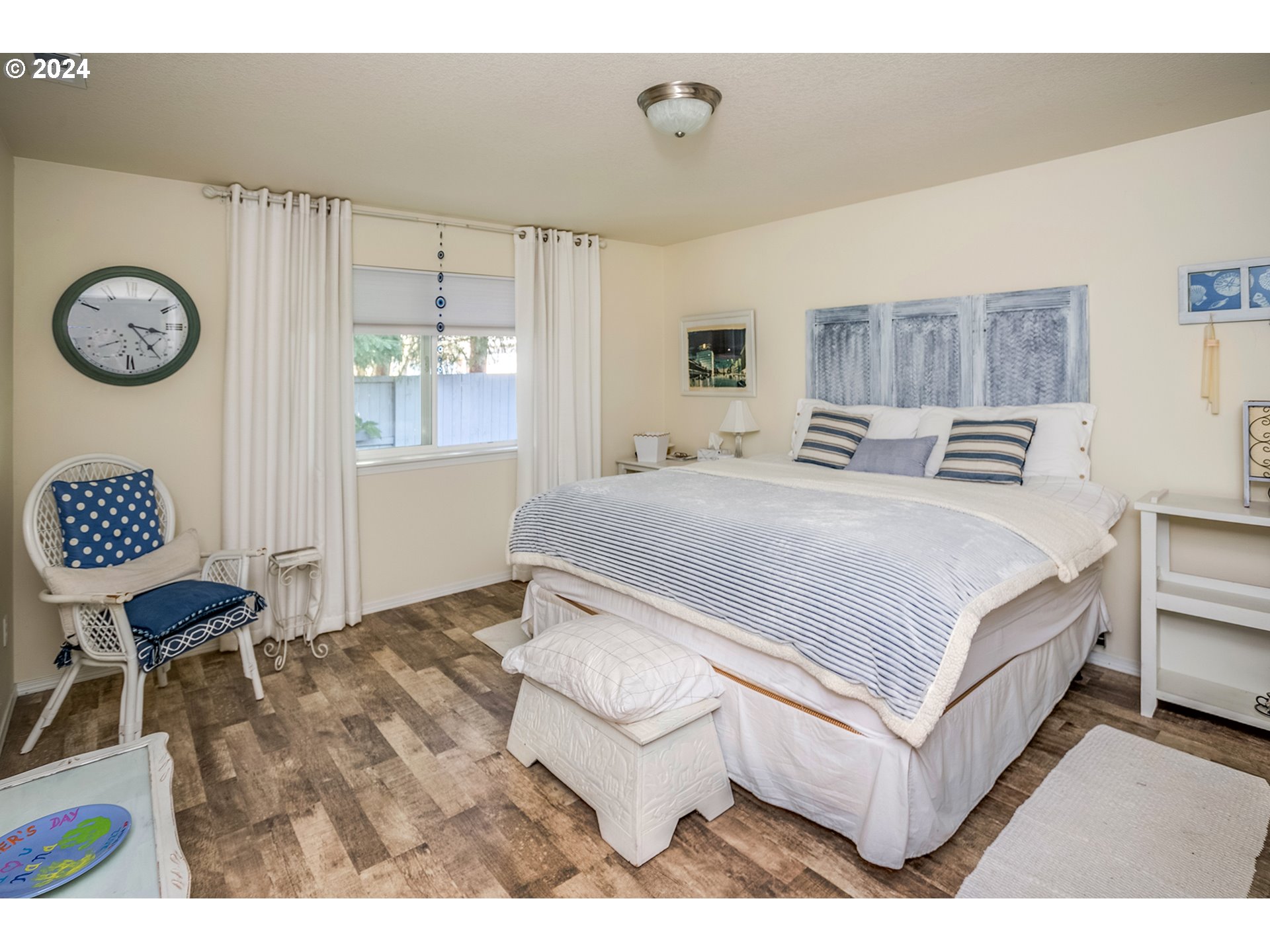 Bedroom with a large striped bed, blue-and-white decor, and a wicker chair by the window.