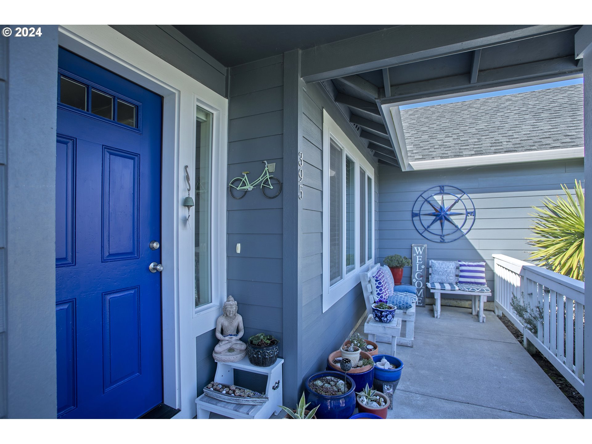 Covered front porch with a vivid blue door, potted plants, and a white bench.