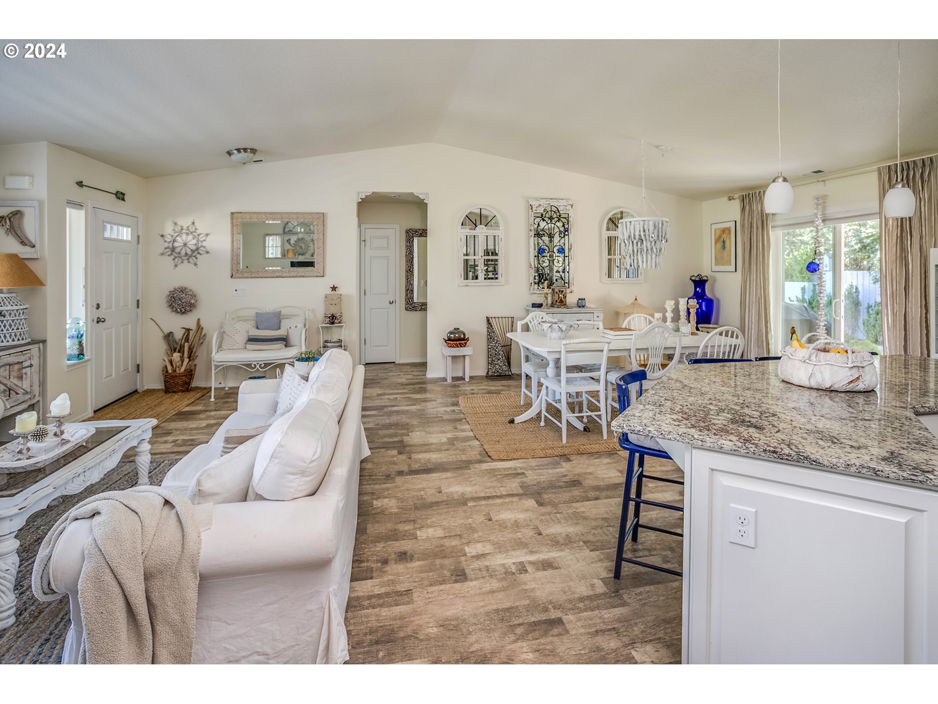 Open-plan living and dining area with white furnishings, a granite kitchen island, and blue bar stools.
