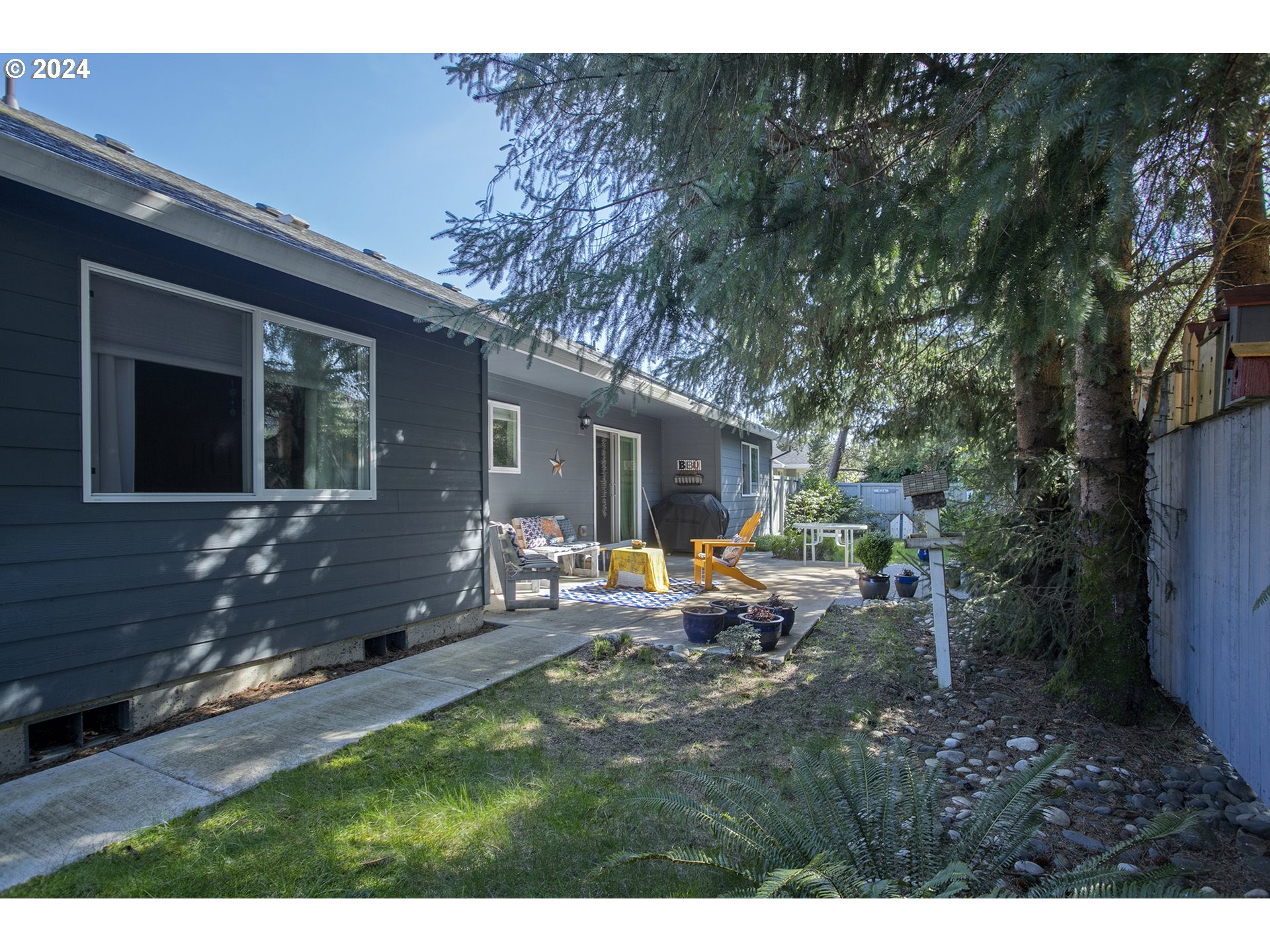 Gray house with a shaded patio furnished with outdoor seating beside a small lawn.