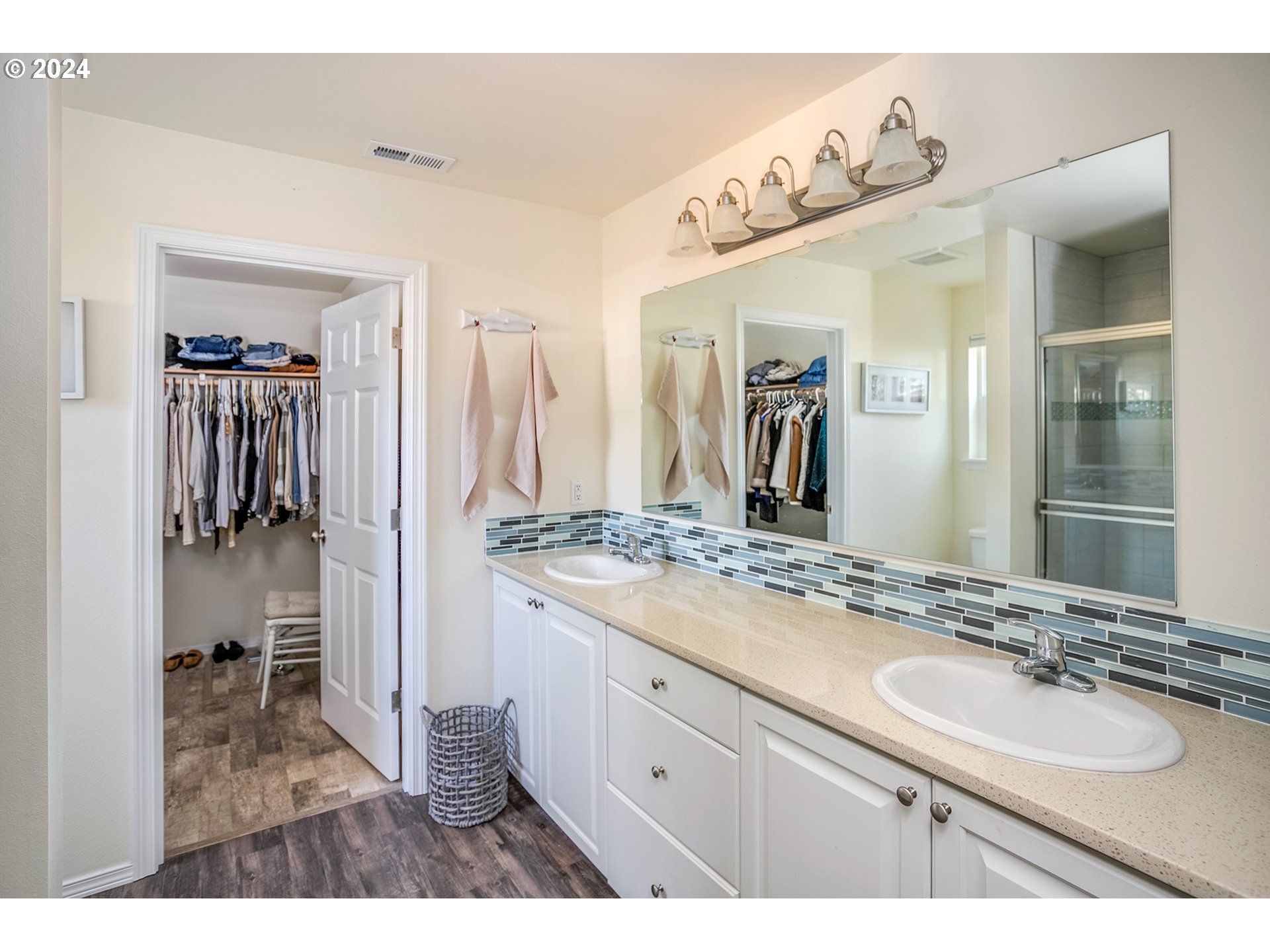 Bathroom with a double-sink vanity, mosaic tile backsplash, and an open doorway to a walk-in closet.