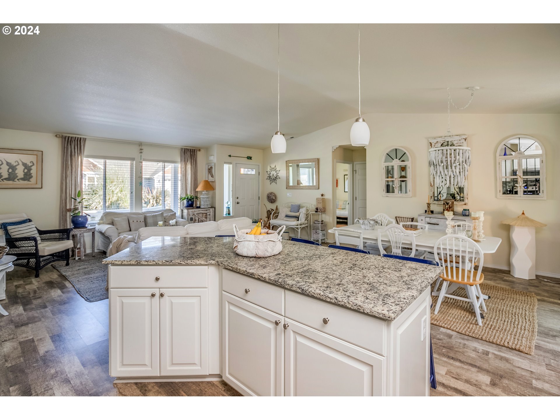Open-plan kitchen with a large granite island, dining table, and living area by bright windows.