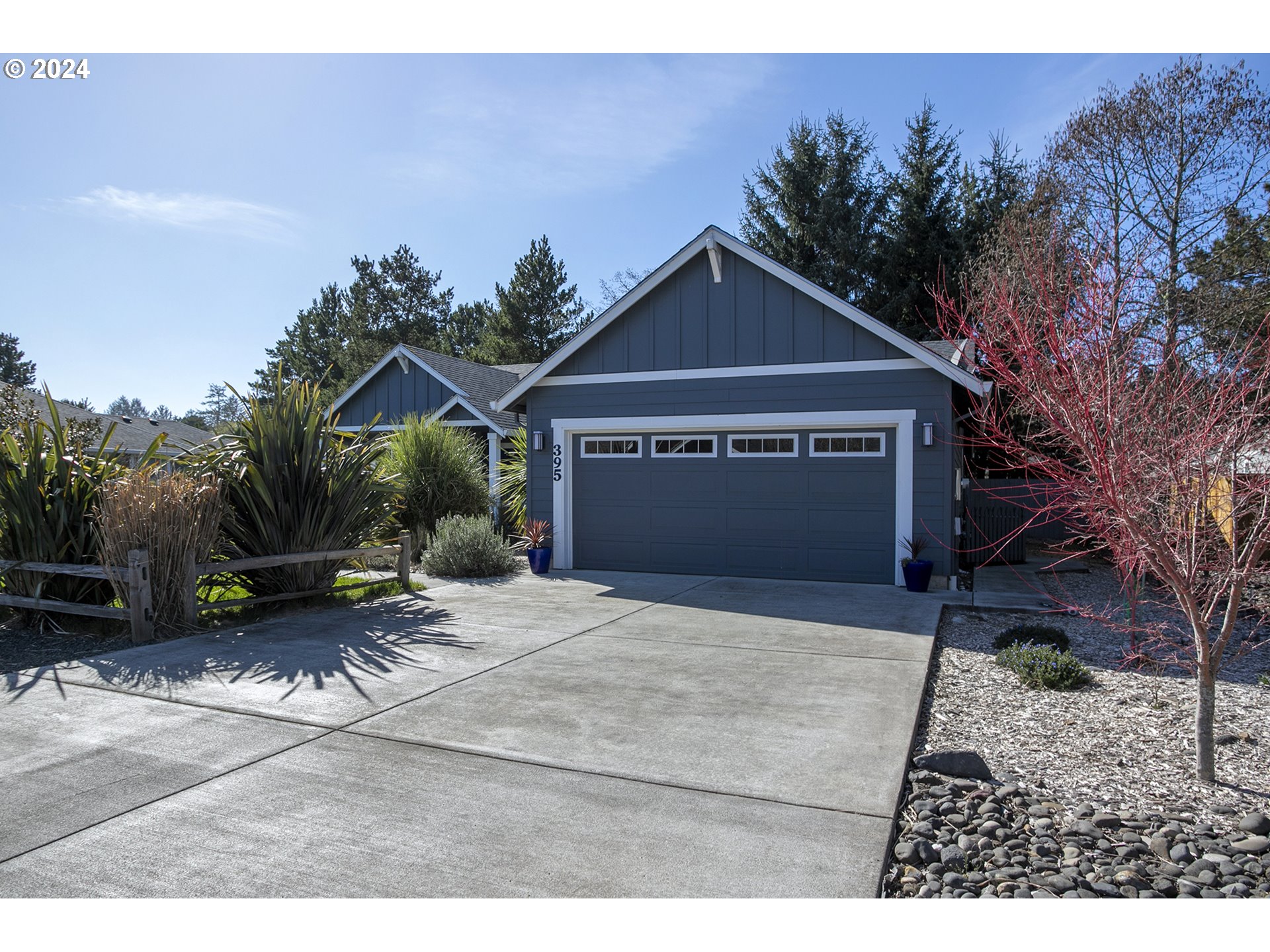 Blue-gray home with a large garage, broad concrete driveway, and landscaped front yard.