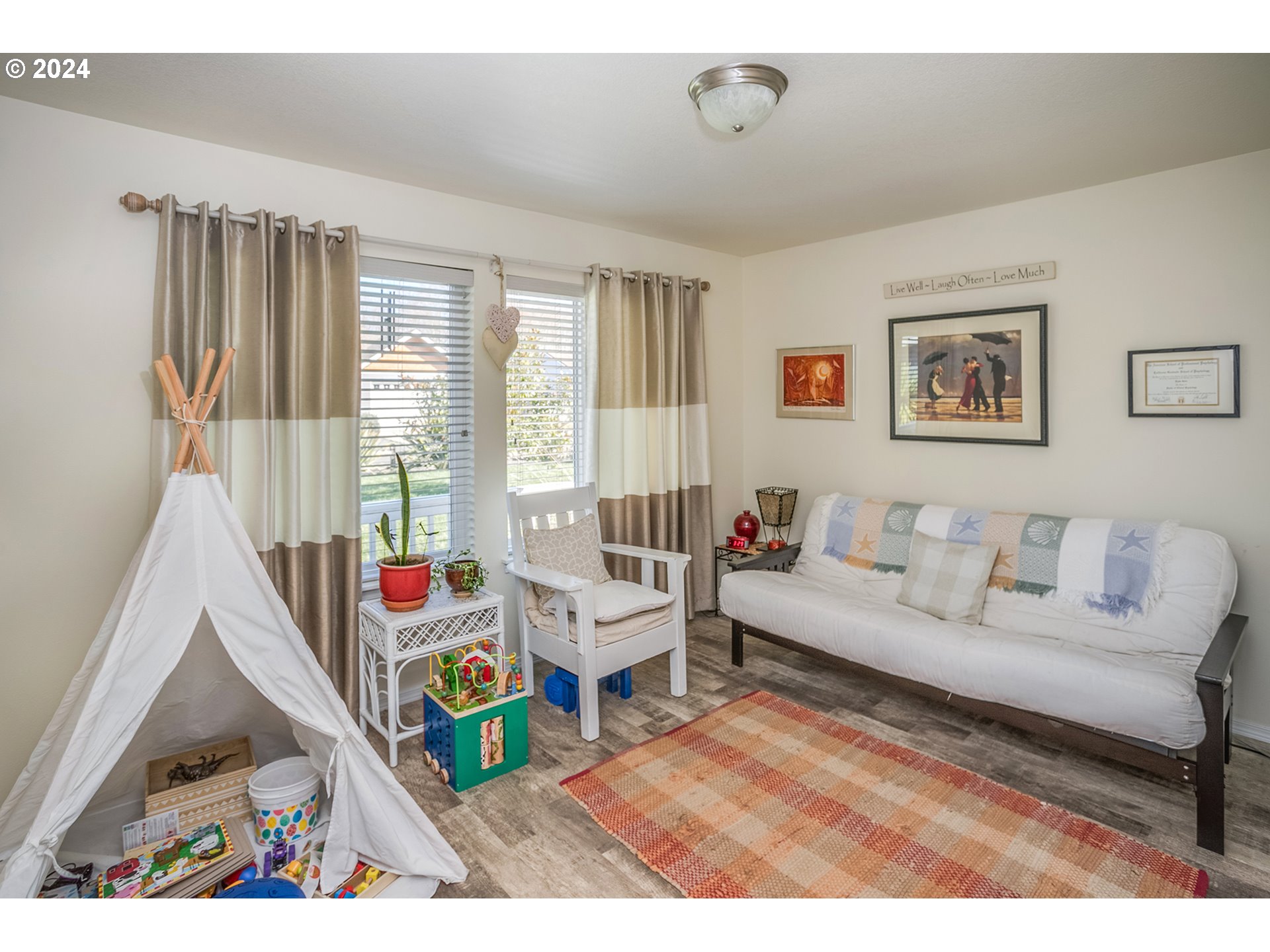 Furnished living room with a white futon, child’s teepee, toys, and colorful rug.