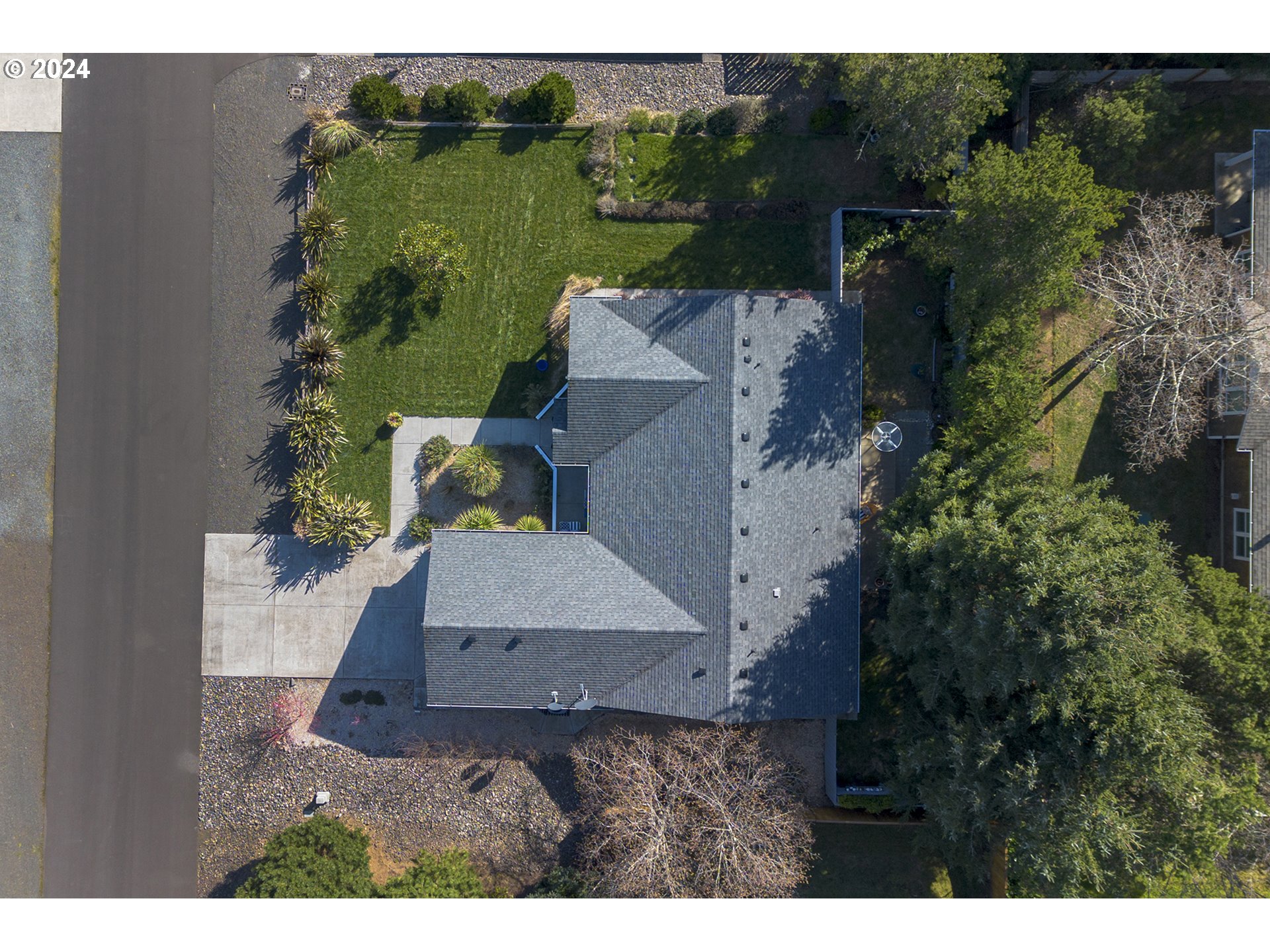 Aerial view of a home with a gray shingle roof, landscaped yard, and surrounding trees.