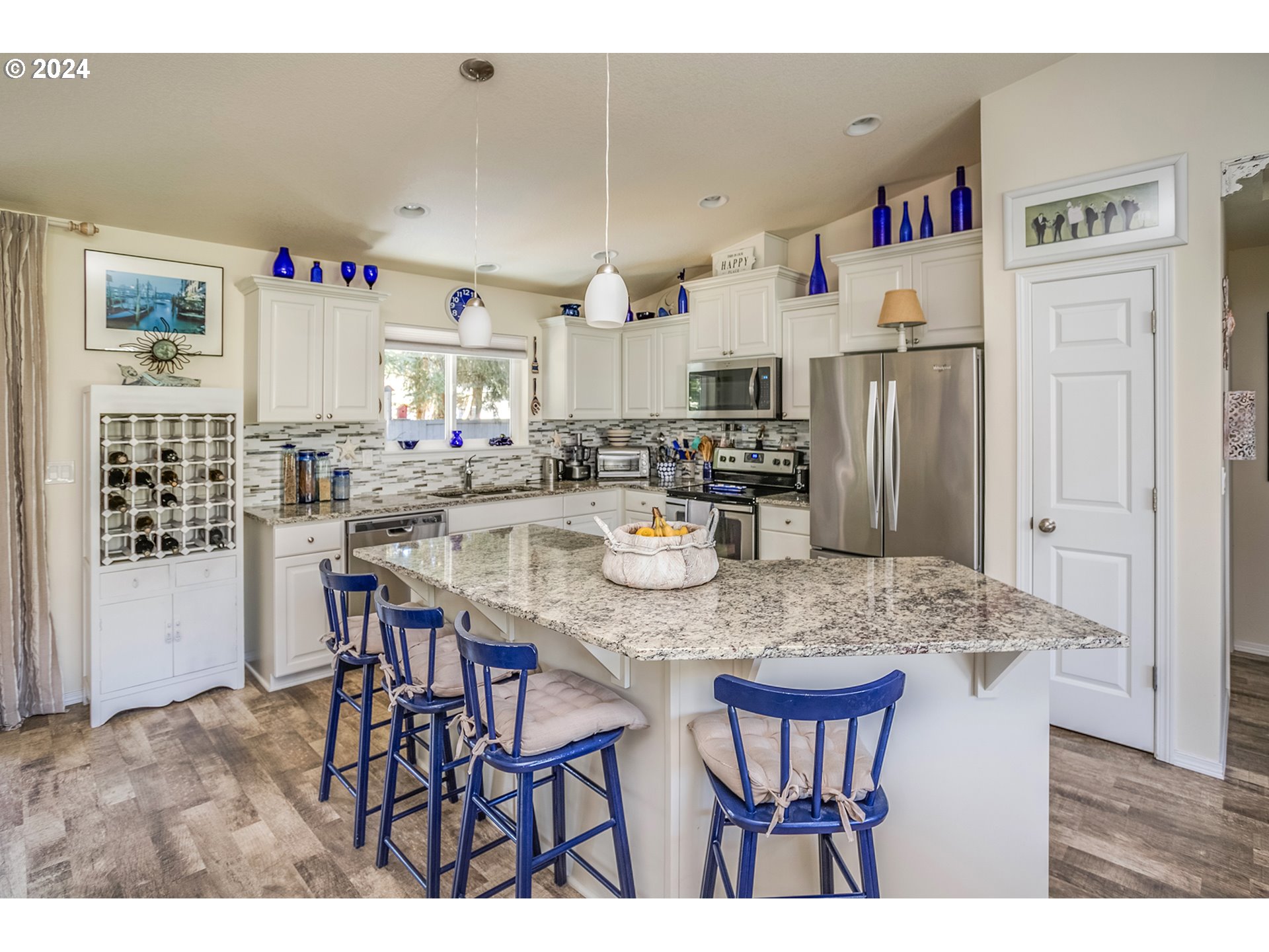 Kitchen with a large granite island, blue bar stools, white cabinetry, and stainless steel appliances.