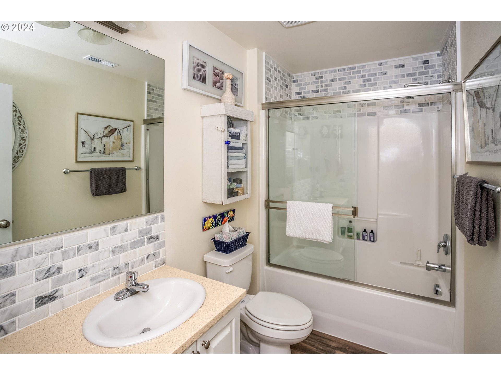 Bathroom with a glass-enclosed tub, gray-and-white tile, and white vanity.