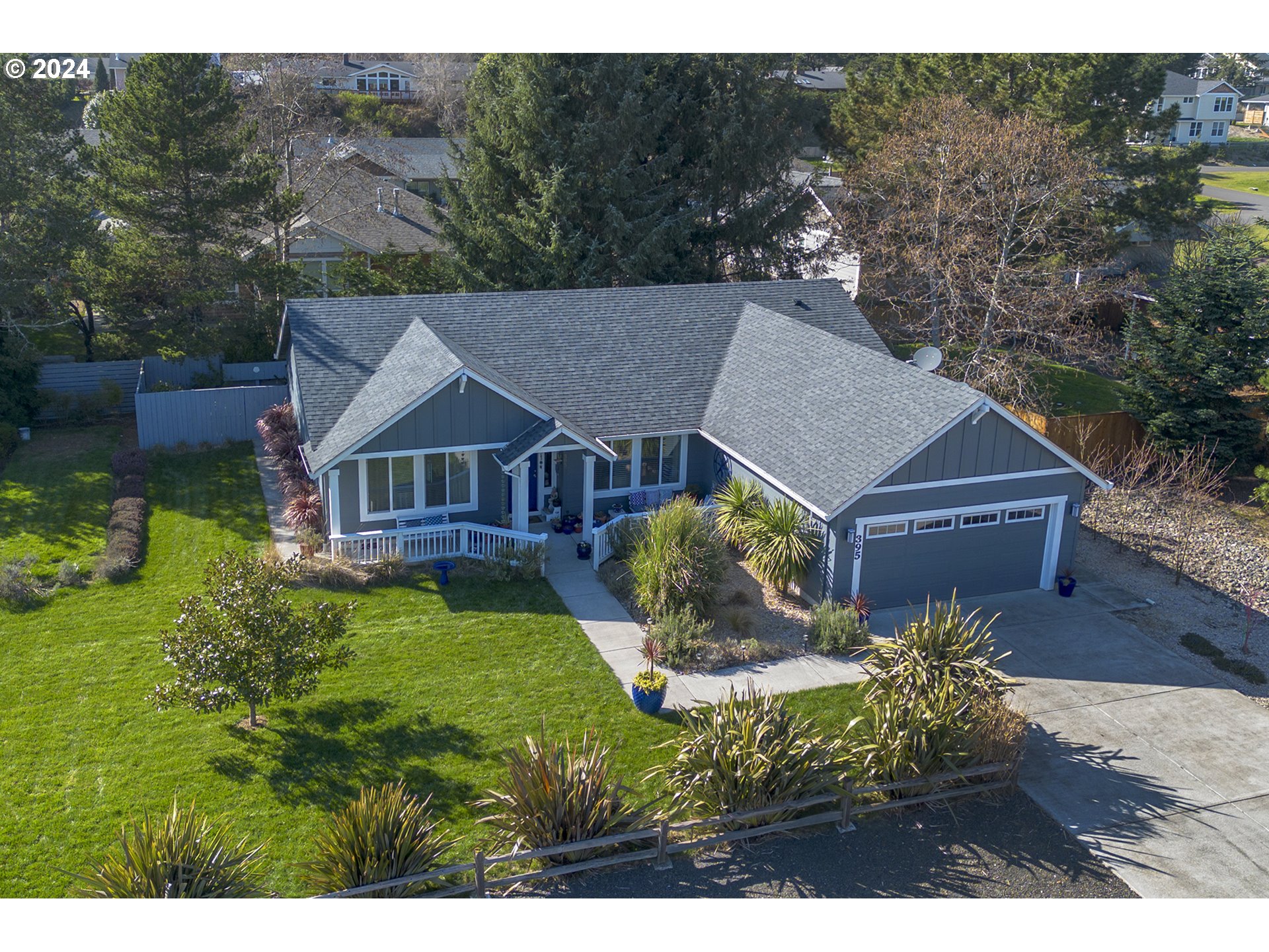 Aerial view of a gray single-story home with a two-car garage, front porch, and landscaped yard.