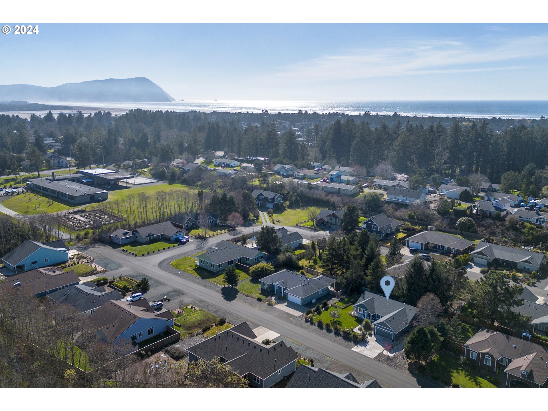 Aerial neighborhood view with a map pin marking a house, the ocean, and a headland beyond.