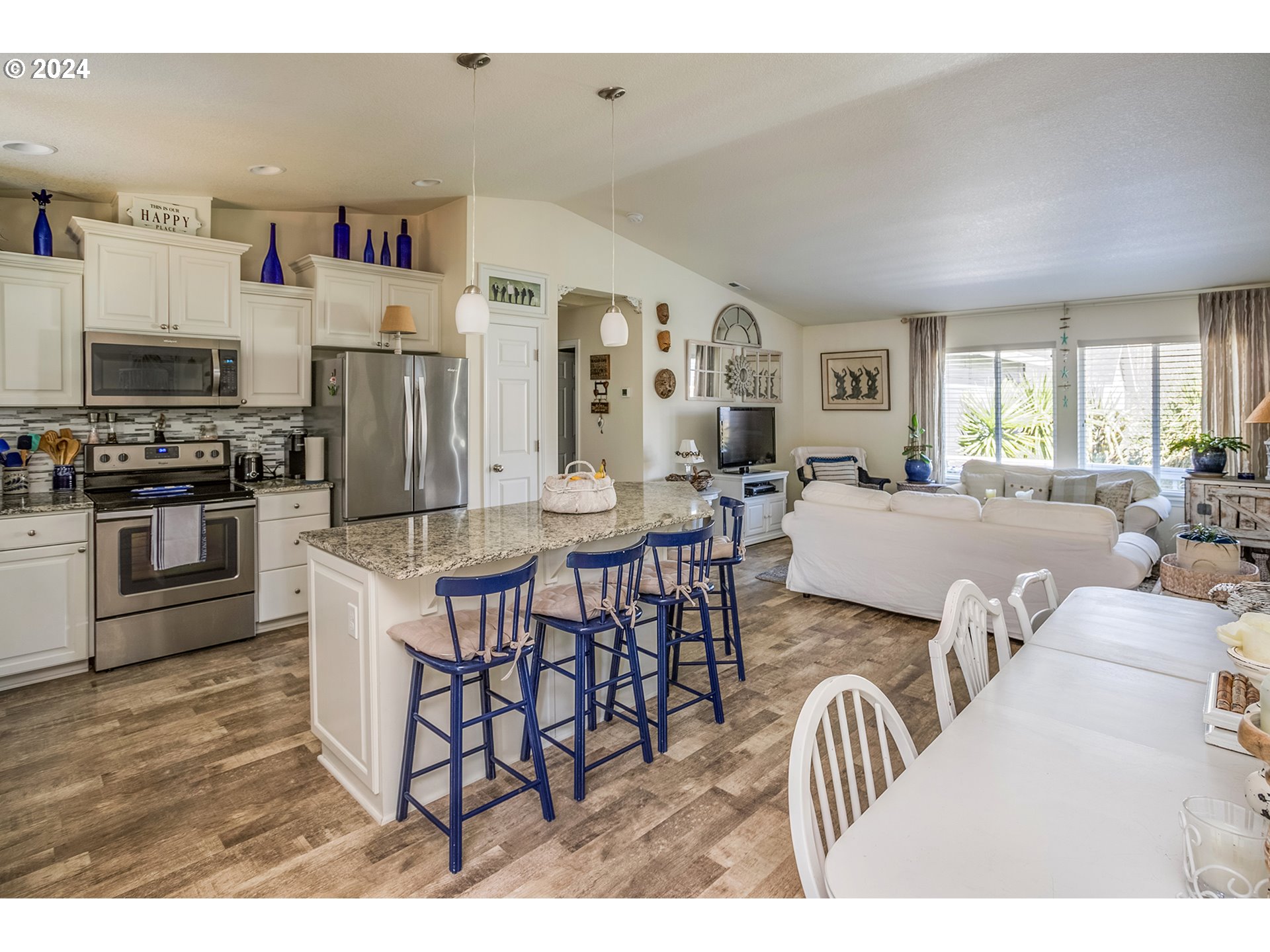 Open-plan kitchen with granite island and blue stools beside the dining and living areas.