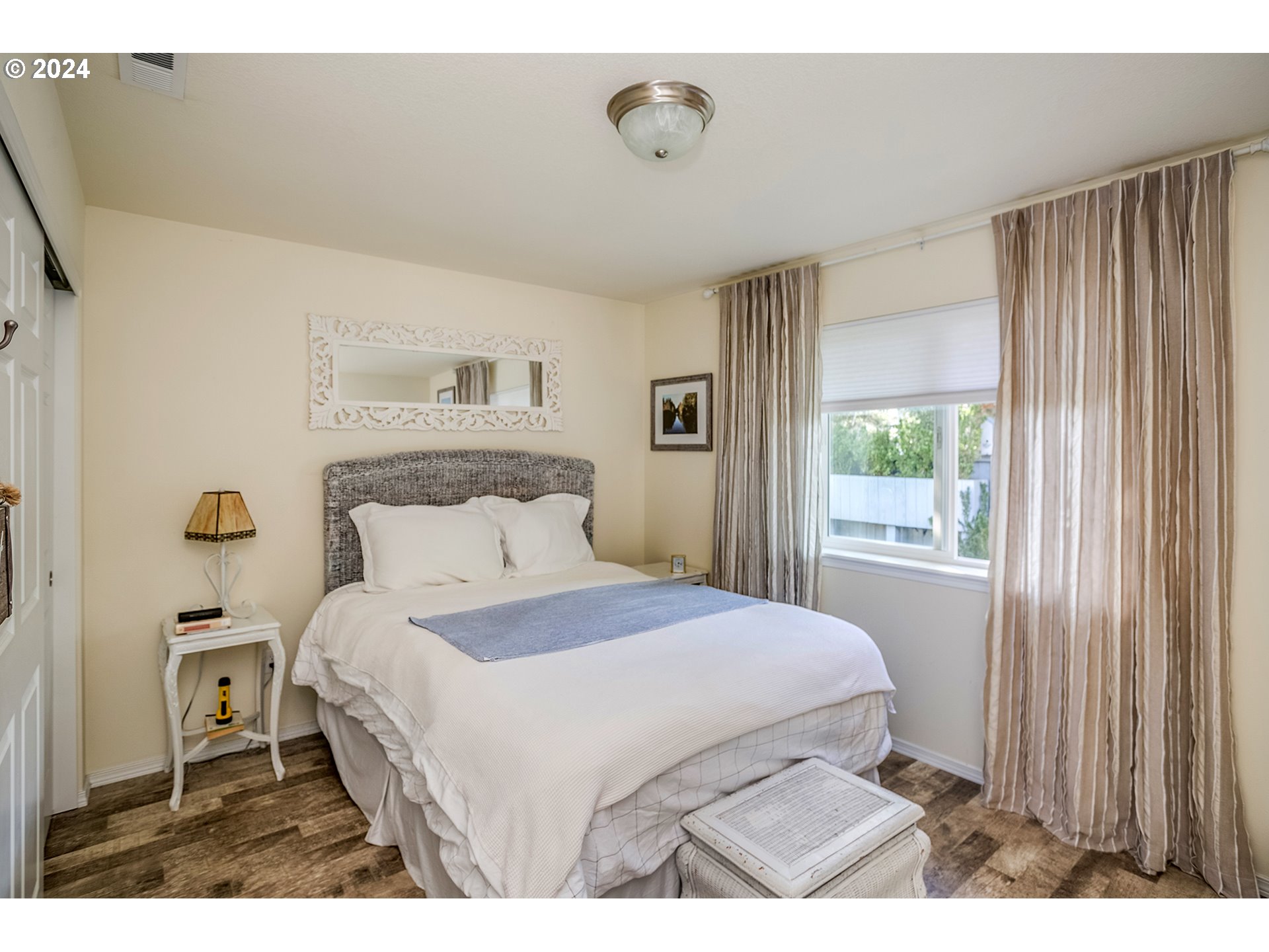 Bedroom with a white bed, ornate mirror, and tall taupe curtains beside the window.