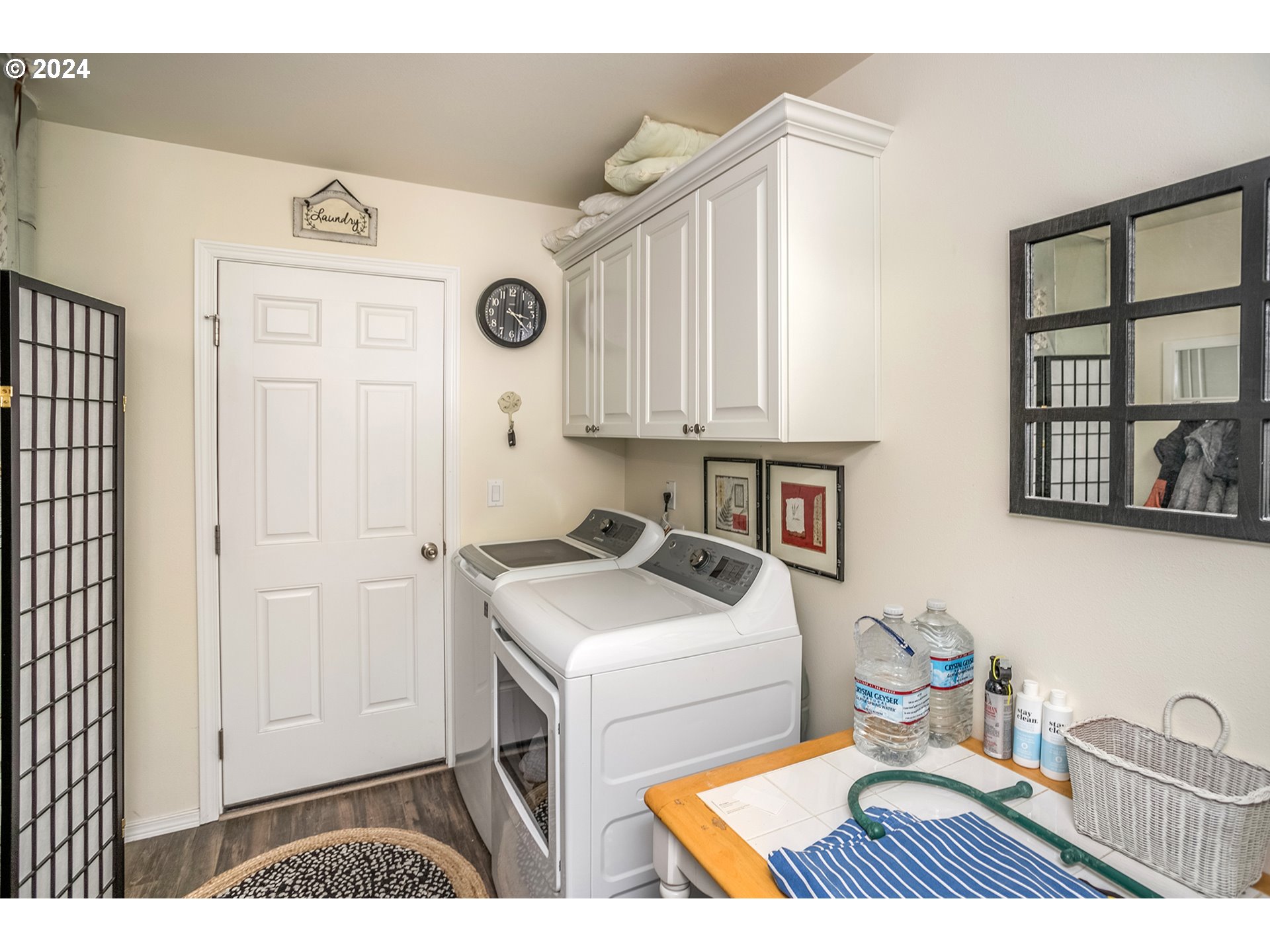 Laundry room with white washer and dryer, overhead cabinets, and a tiled folding counter.