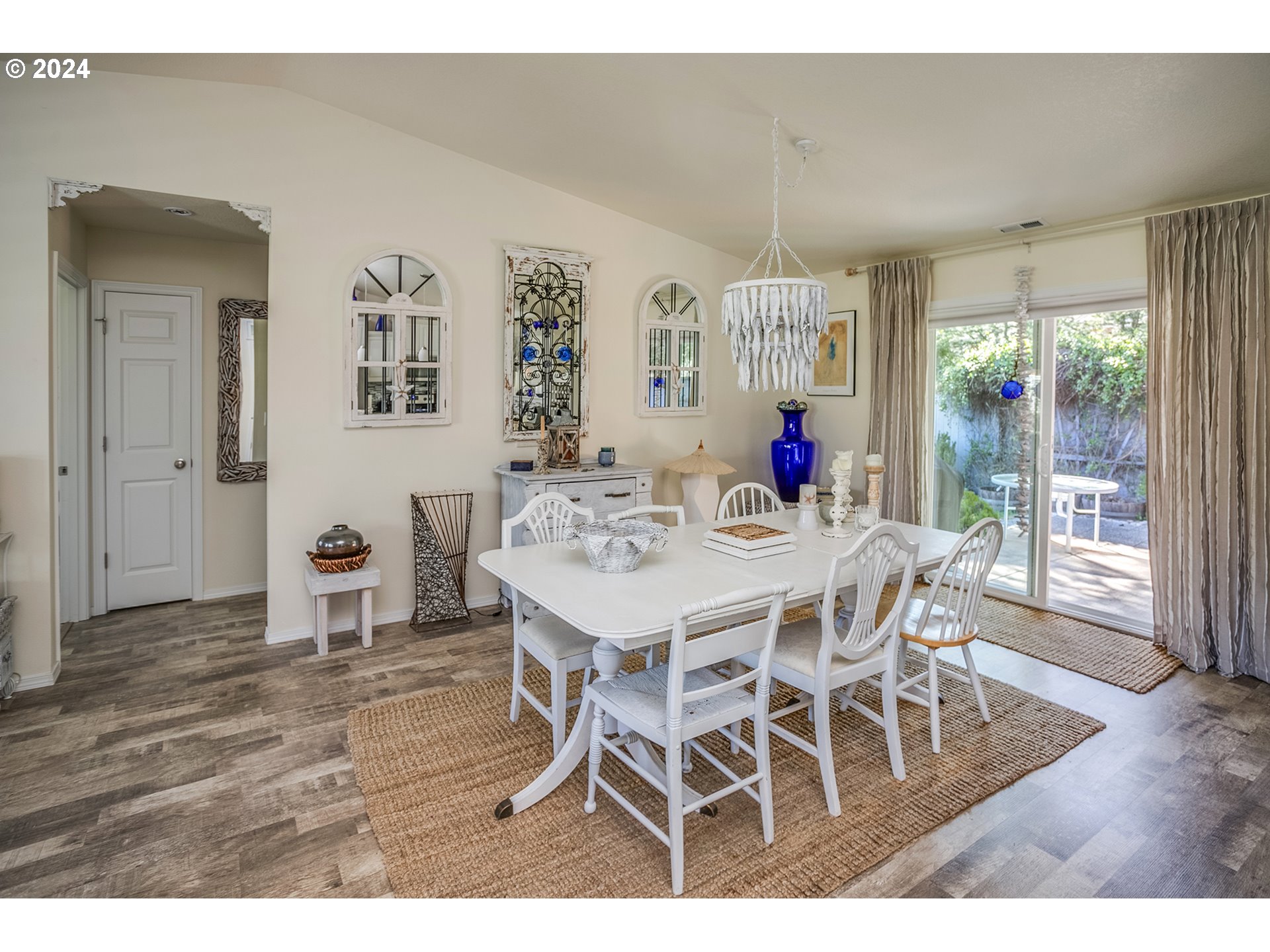 Dining room with a white table, decorative chandelier, and sliding glass doors to a patio.