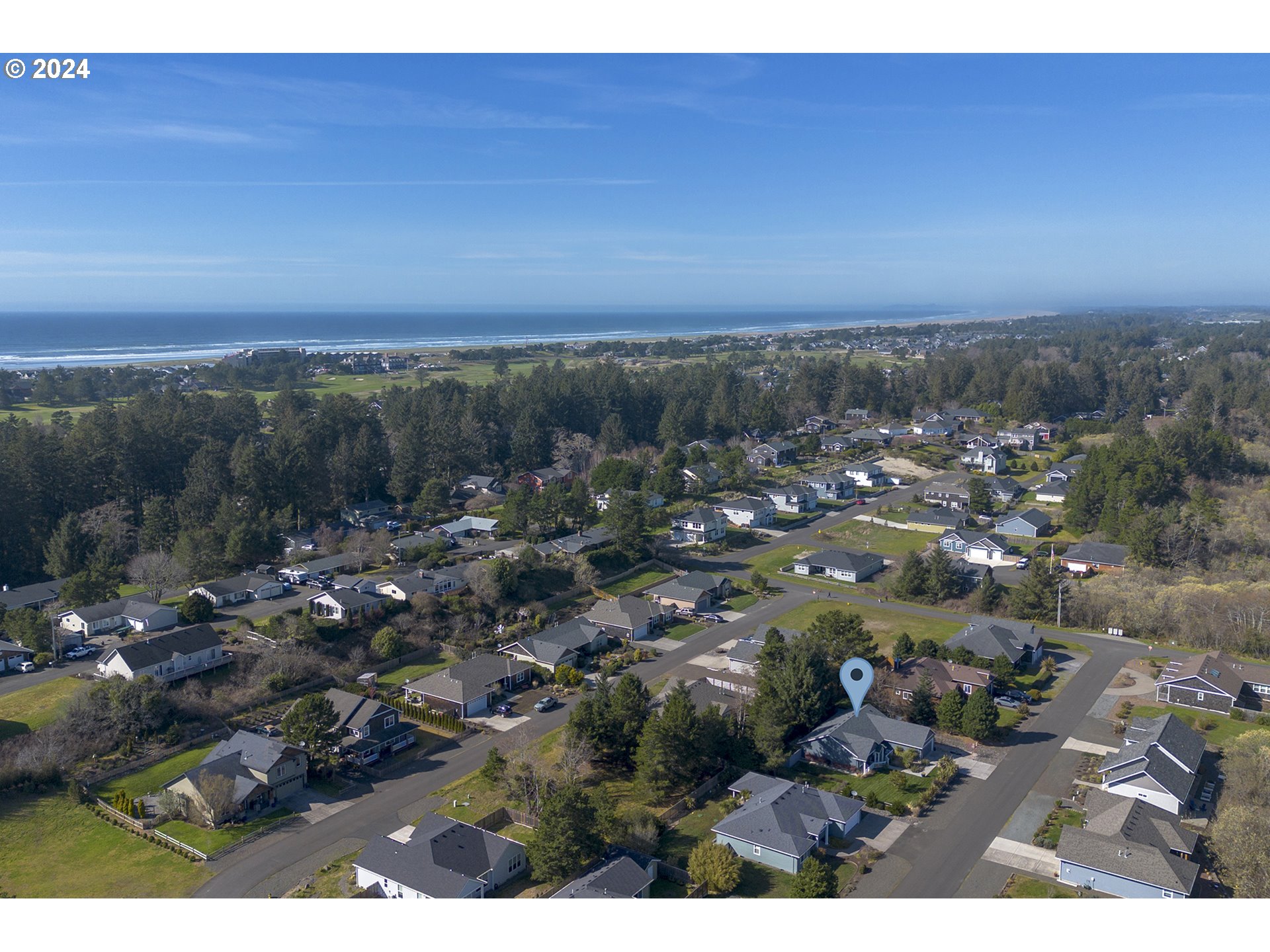 Aerial view of a coastal neighborhood and ocean, with a map pin marking the property.