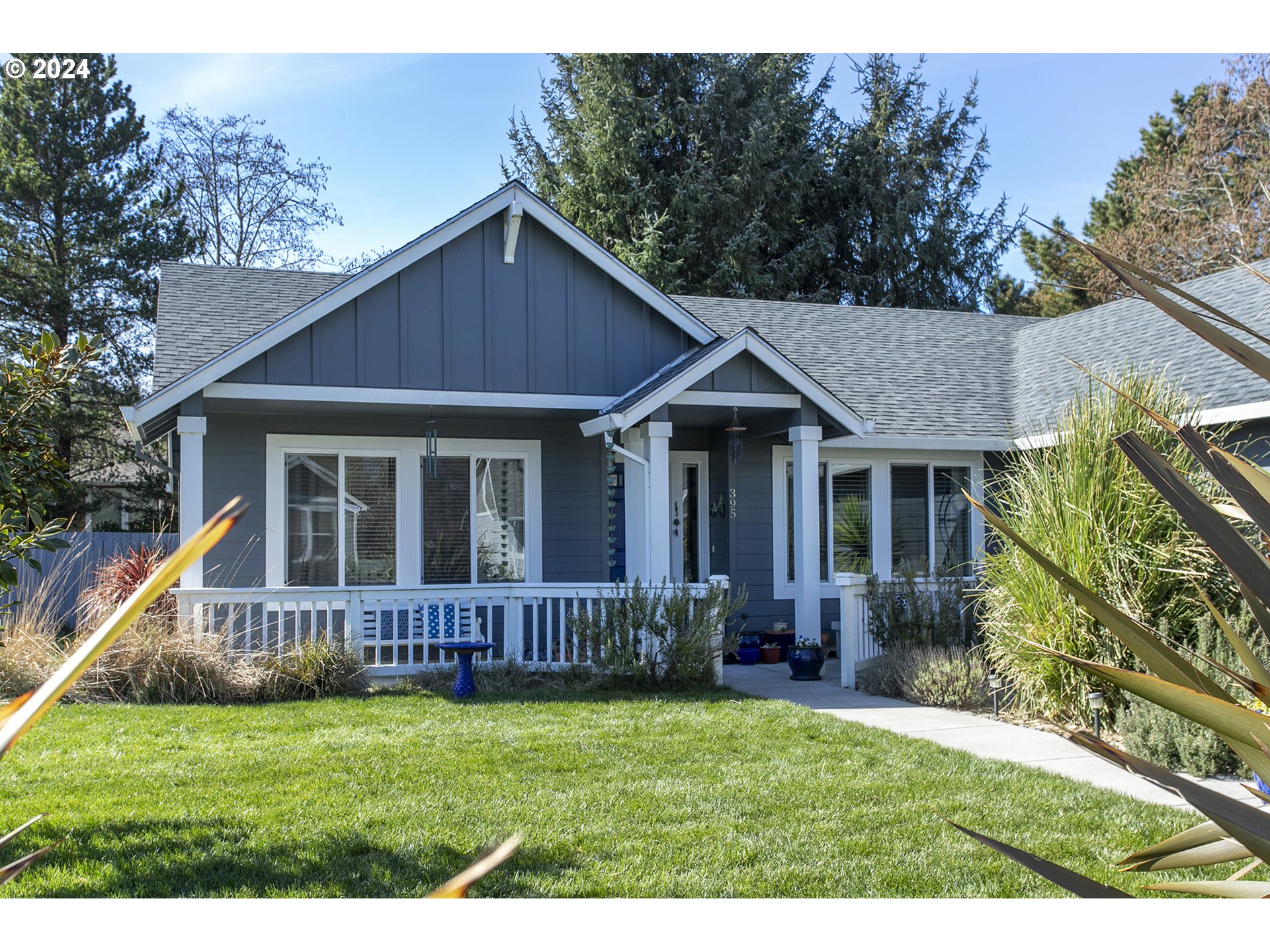 Blue-gray house with white-trimmed covered porch and landscaped front lawn.