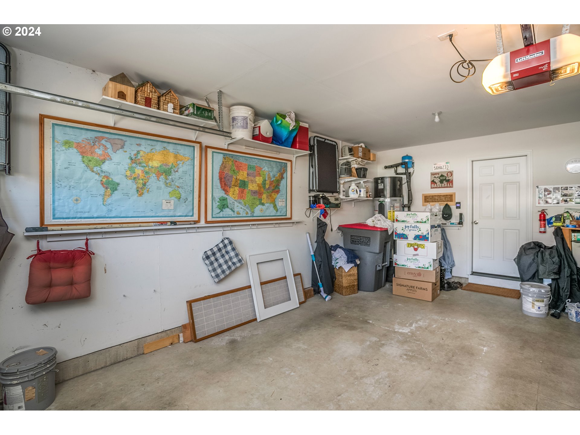 Garage with wall-mounted maps, storage shelves, boxes, and a concrete floor.