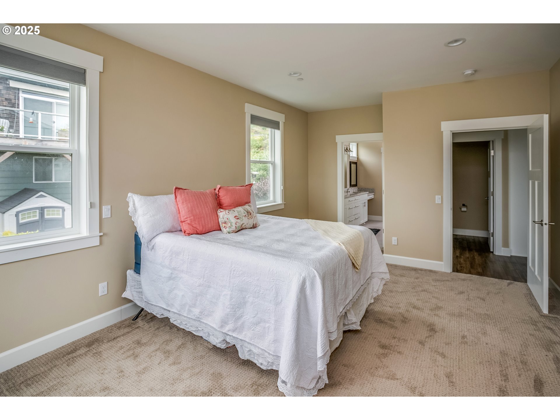 Bedroom with a white bed and coral pillows, two windows, and an open doorway to the bathroom.