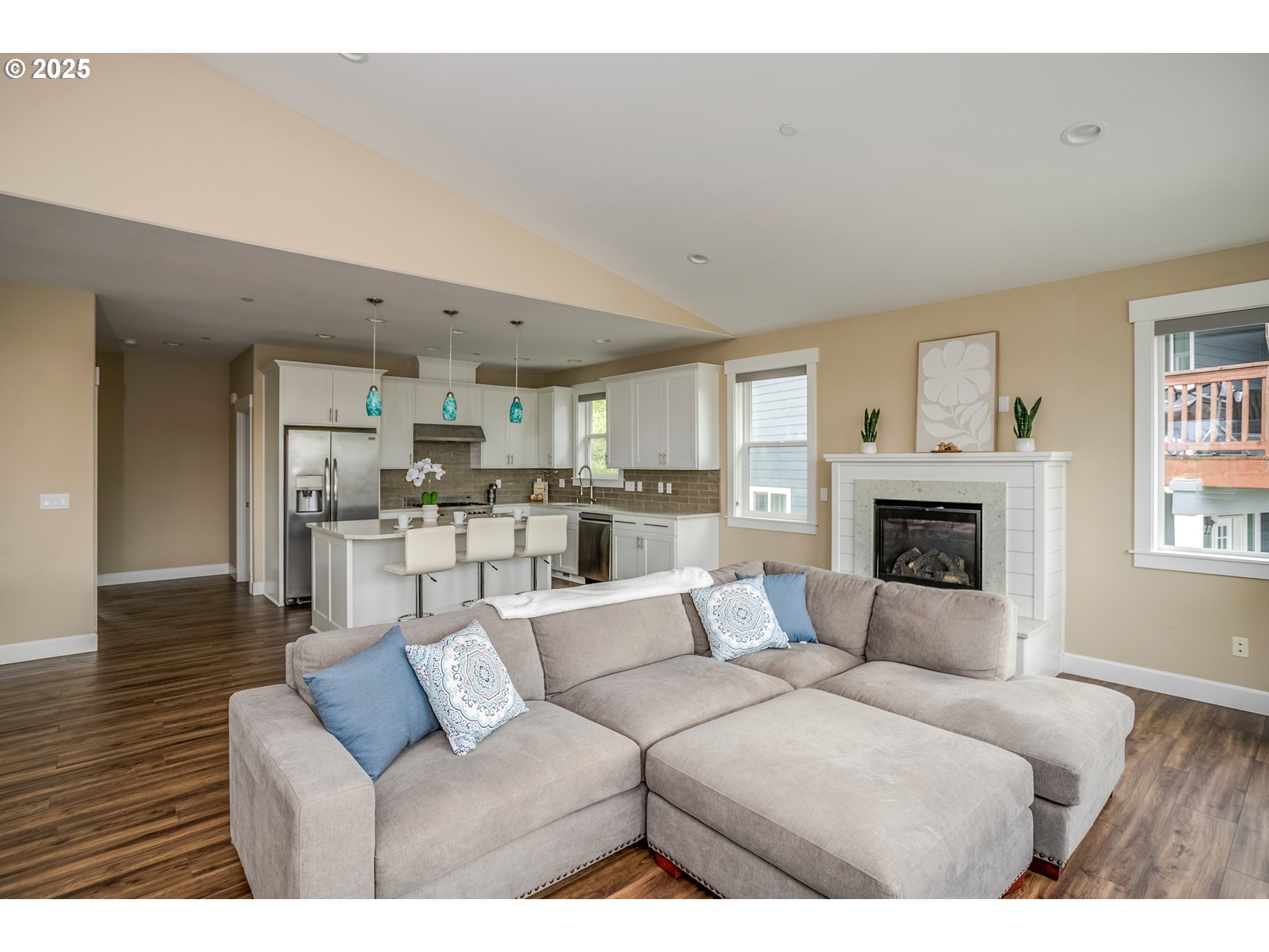Open-plan living room and kitchen with a large sectional, white cabinetry, wood floors, and a fireplace.