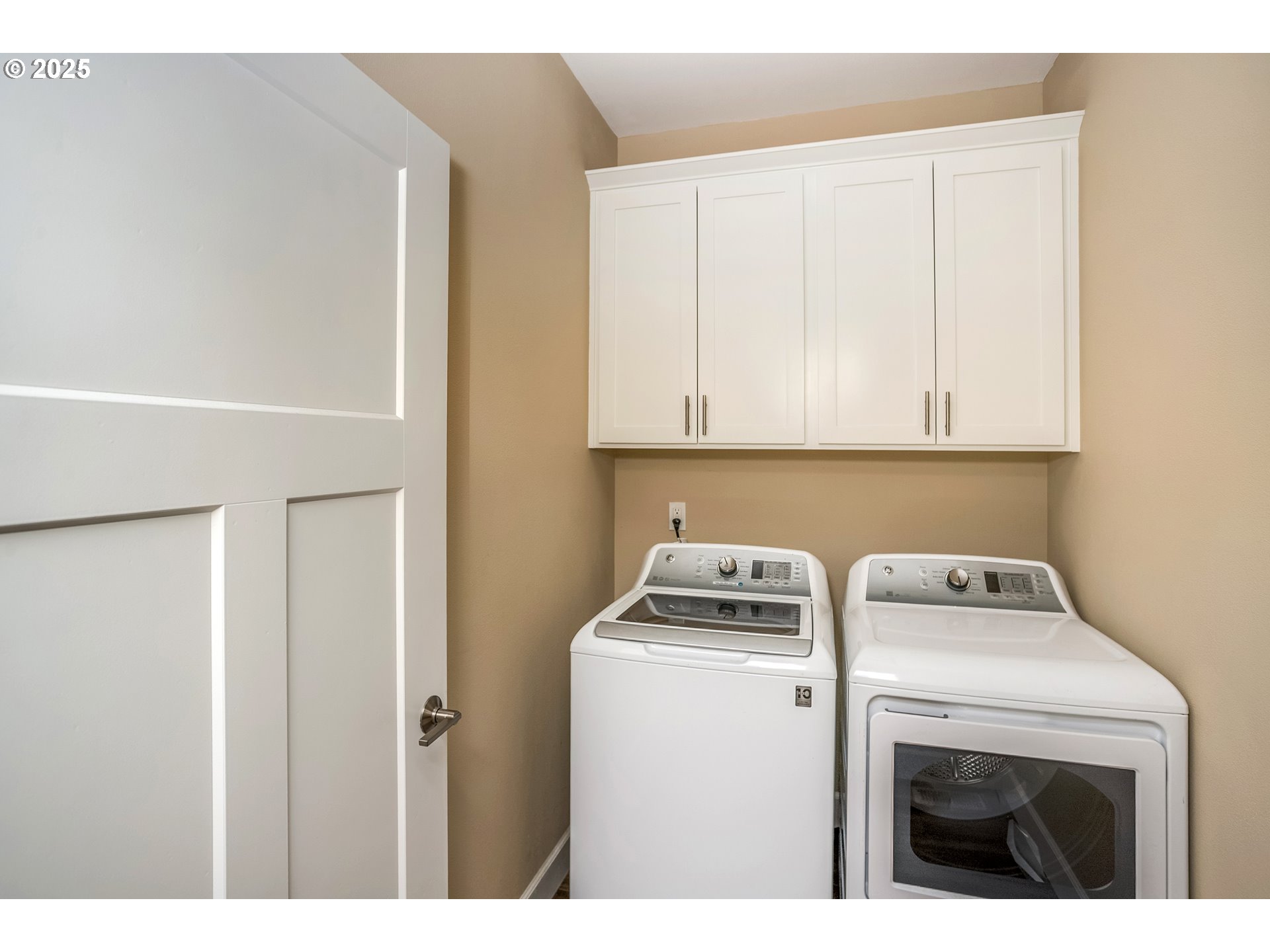 Laundry room with a top-load washer, front-load dryer, and white overhead cabinets.