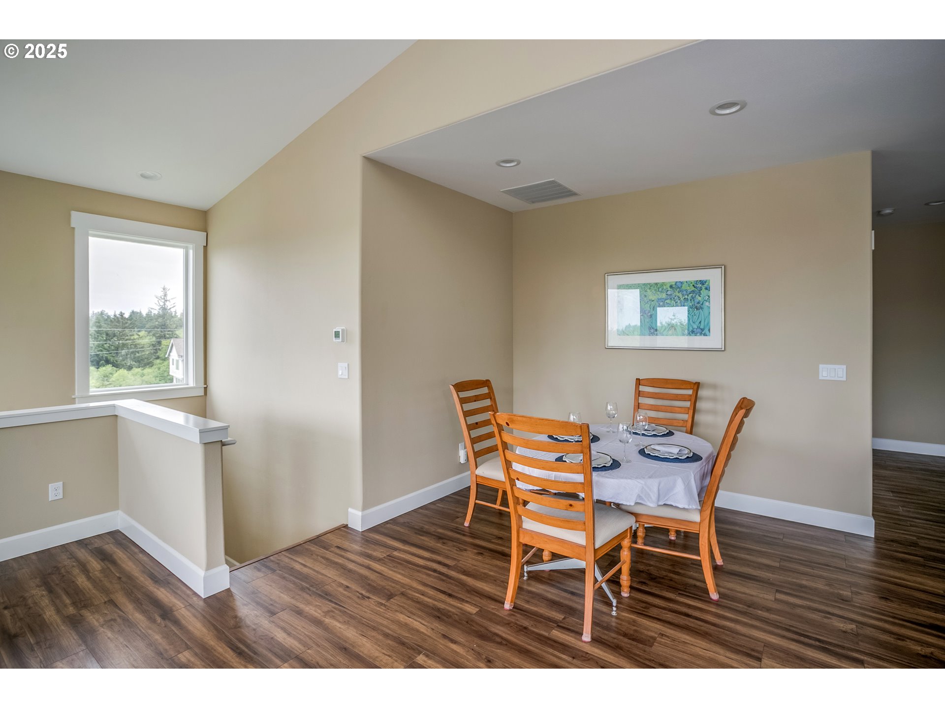 Dining area with a set table, wooden chairs, and a large window overlooking trees.