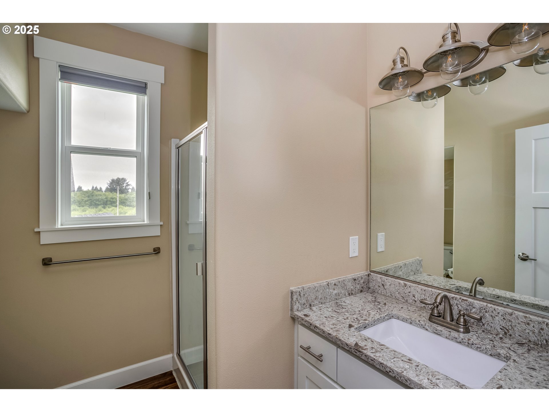 Bathroom with a granite vanity, large mirror, glass shower, and window.