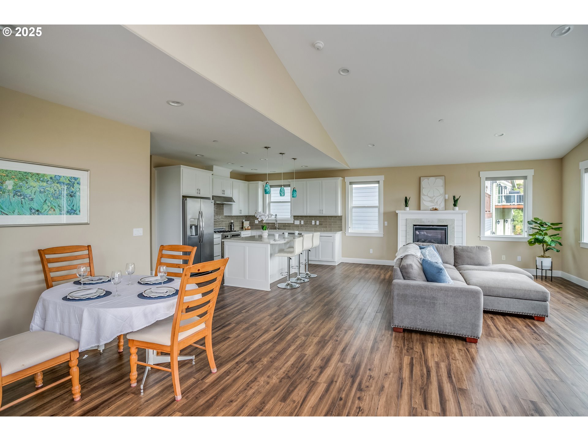Open-concept living and dining room with a white kitchen, island, fireplace, and gray sectional sofa.