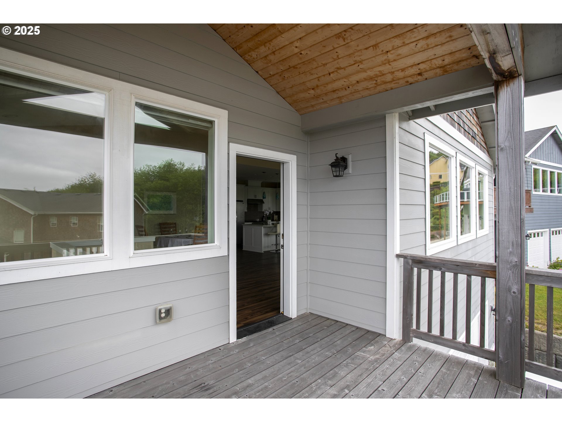 Covered deck with gray floorboards, a wood plank ceiling, and an open doorway.