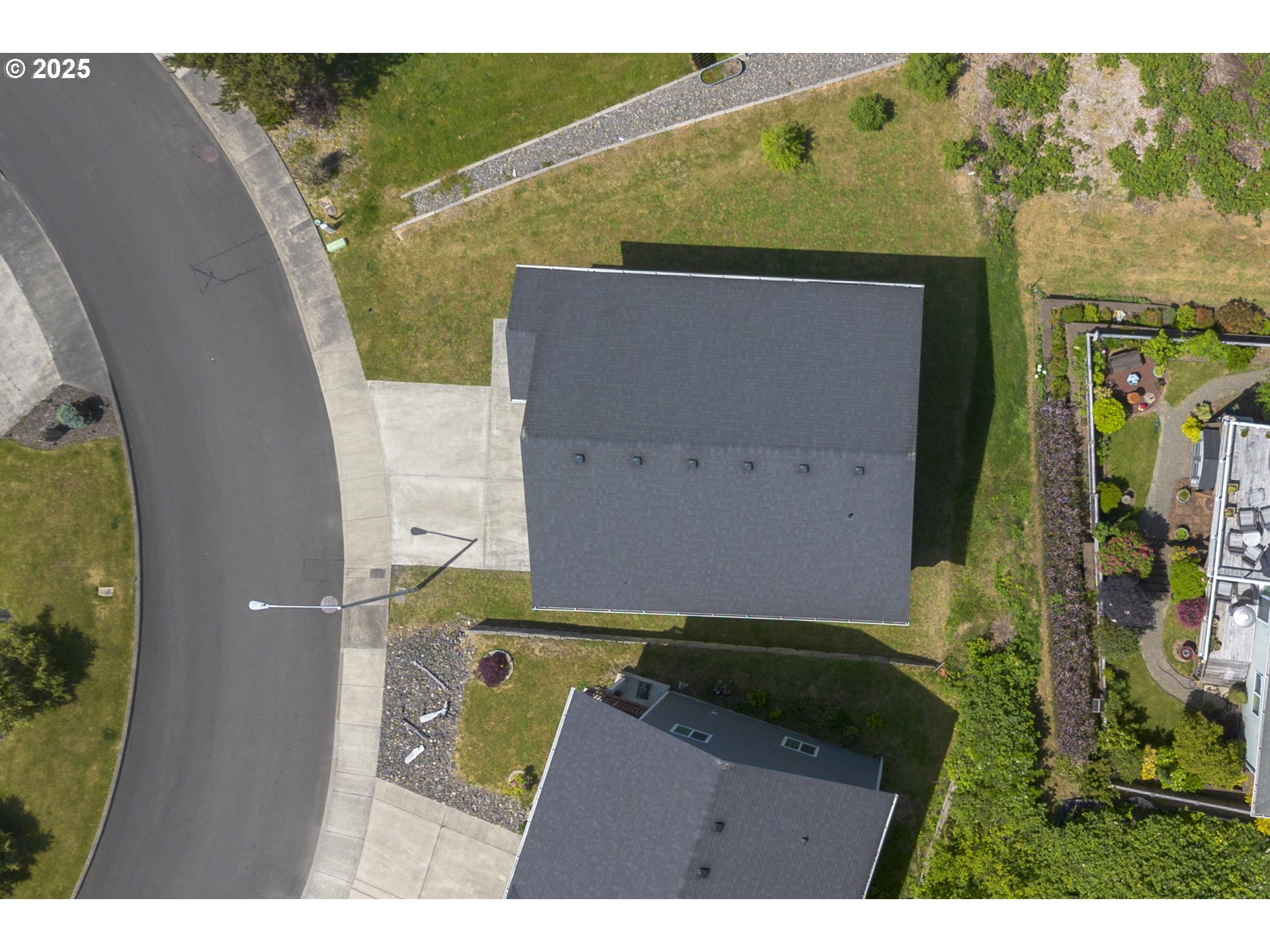 Aerial view of a house with a dark roof beside a curved residential street.
