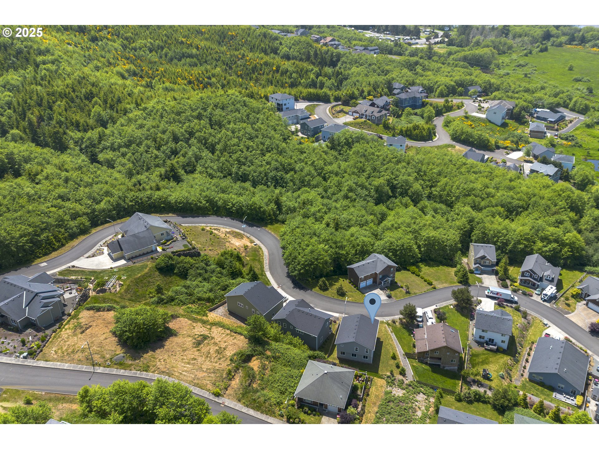 Aerial view of homes along curving streets amid dense green woodland, with a blue location pin.