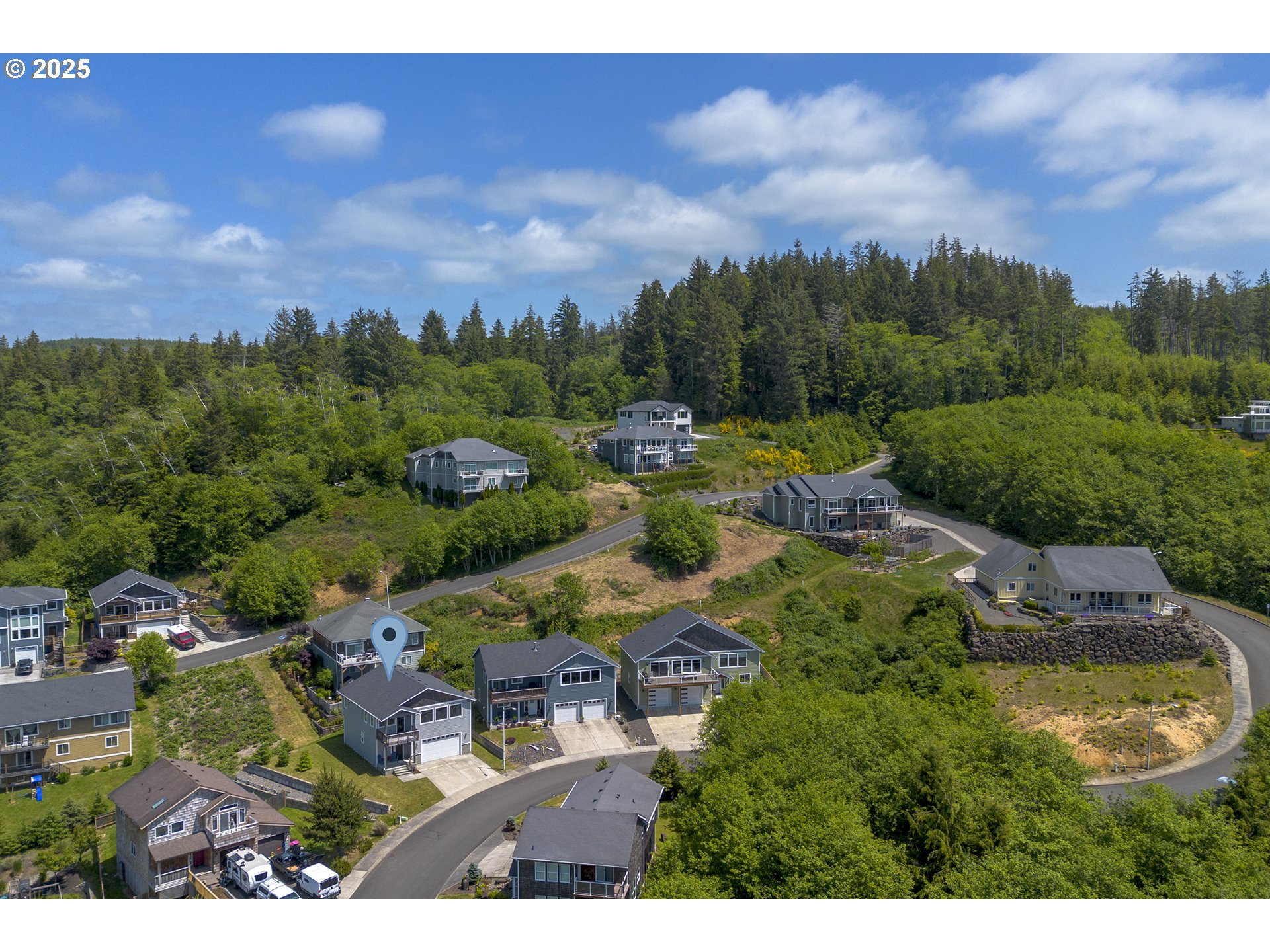 Aerial view of homes among dense woodland, with a map pin marking a gray house.