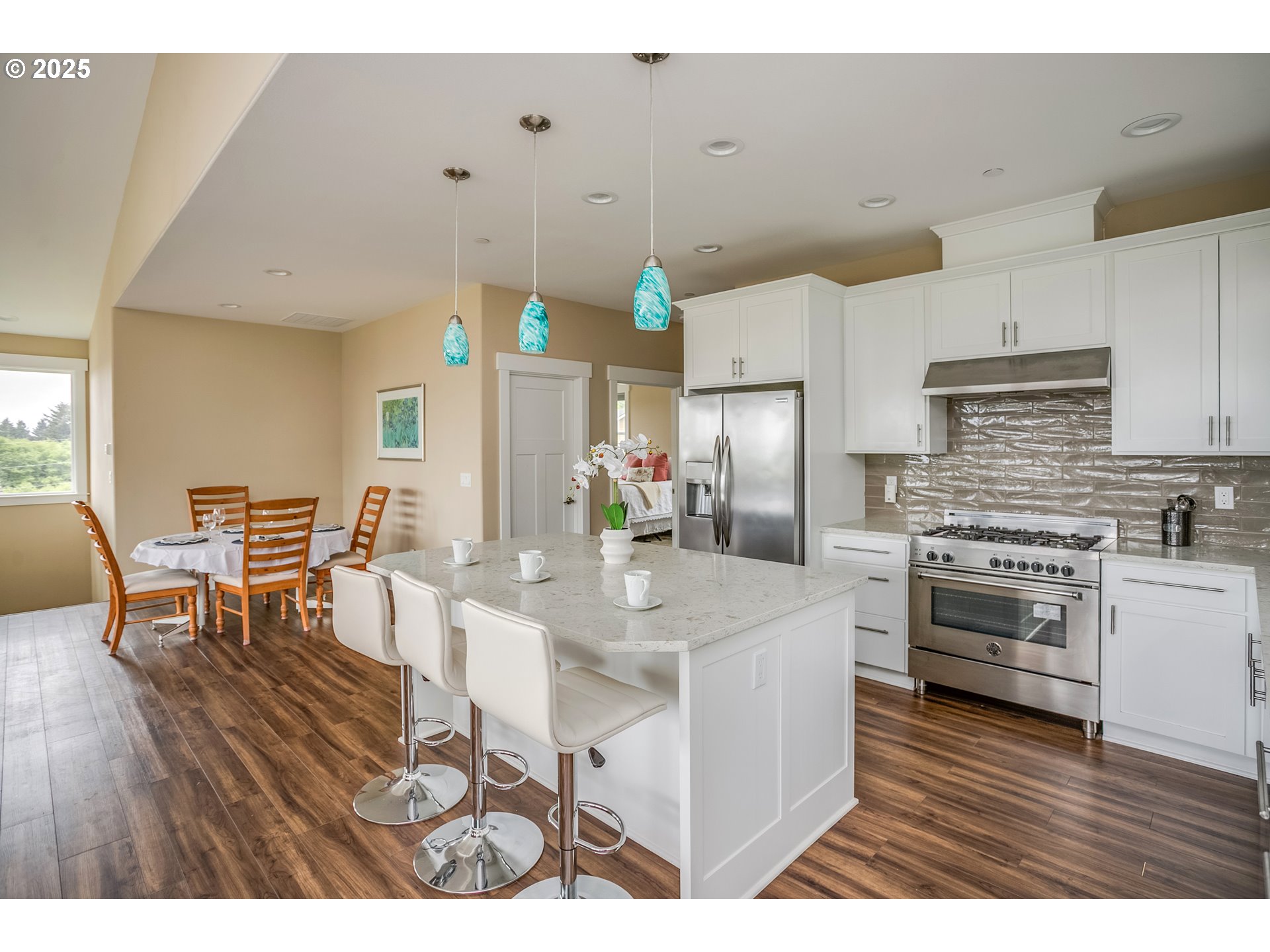 Kitchen and dining area with a large white island, stainless steel appliances, and turquoise pendant lights.
