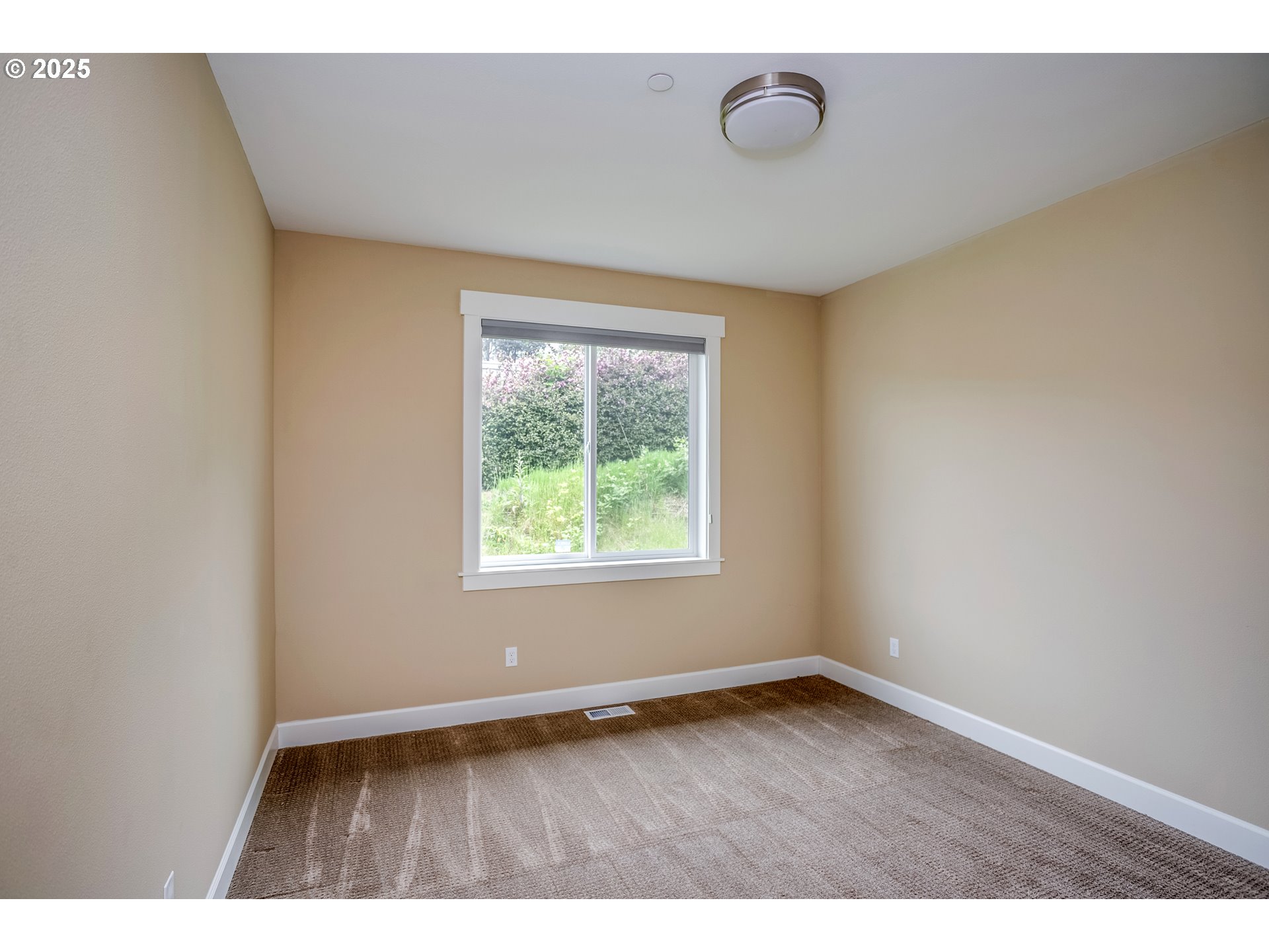 Empty carpeted room with beige walls and a window overlooking greenery.