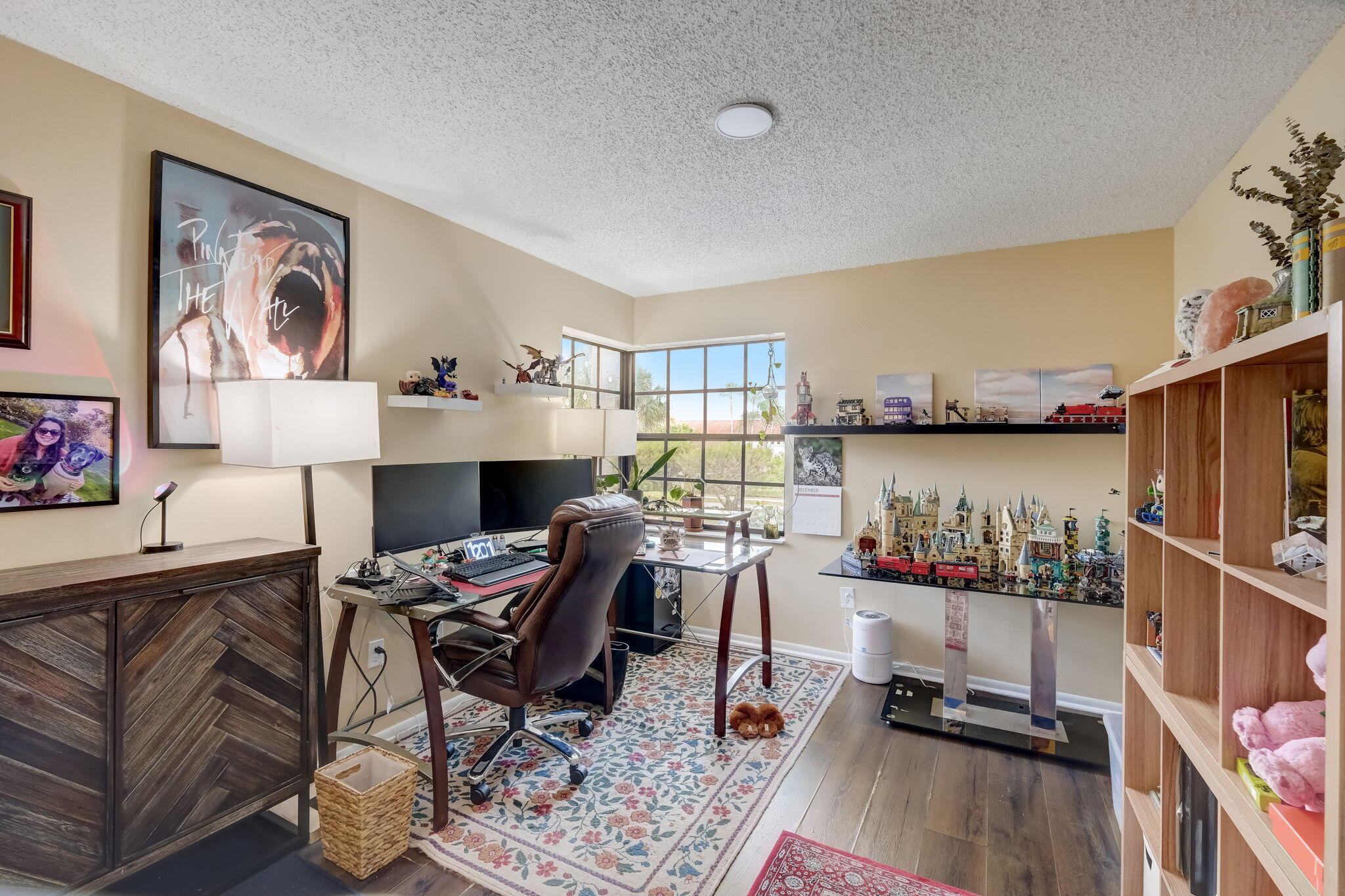 Home office with a computer desk, bright corner windows, and shelves of collectible model buildings and trains.