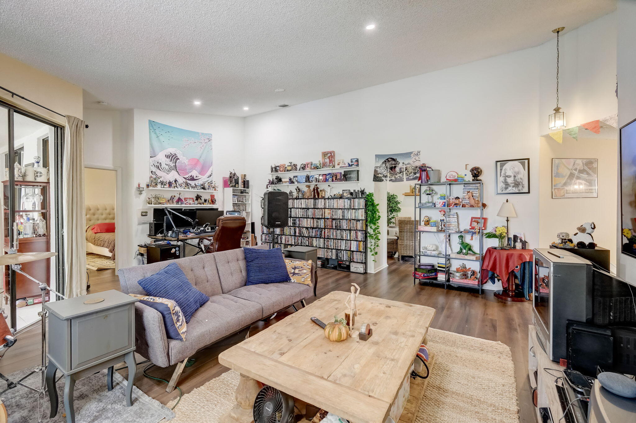 Living room with a gray sofa, large wooden coffee table, and shelves crowded with DVDs and collectibles.