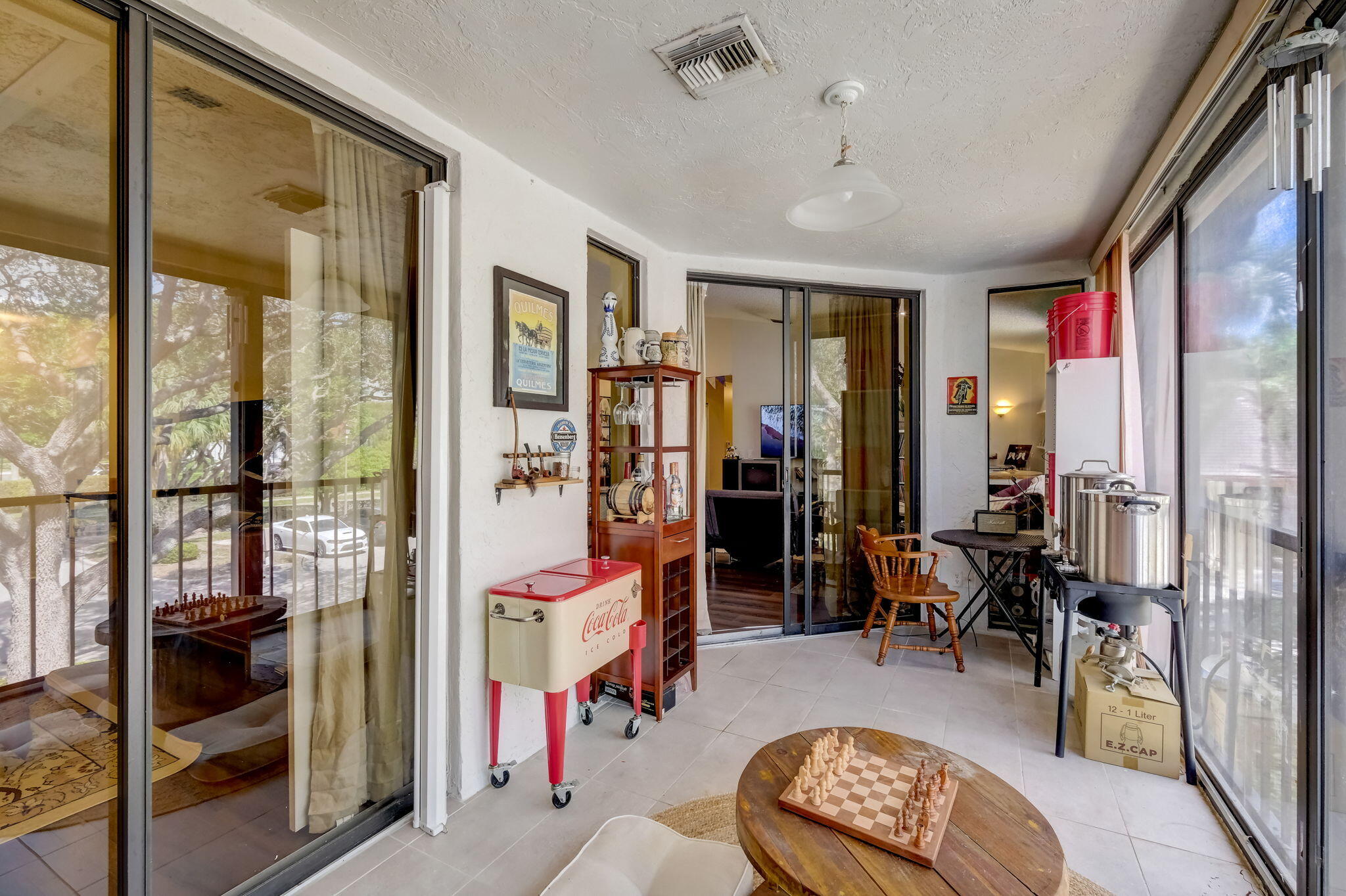 Enclosed sunroom with sliding glass doors, a chess table, vintage Coca-Cola cooler, and bar equipment.