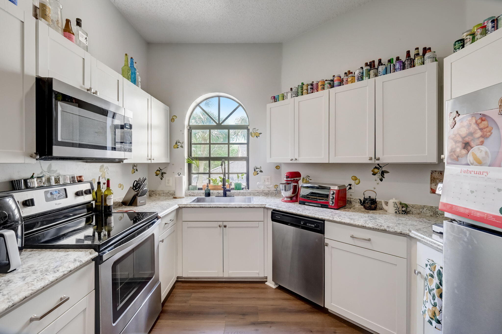 Kitchen with white cabinetry, stainless steel appliances, and an arched window above the sink.