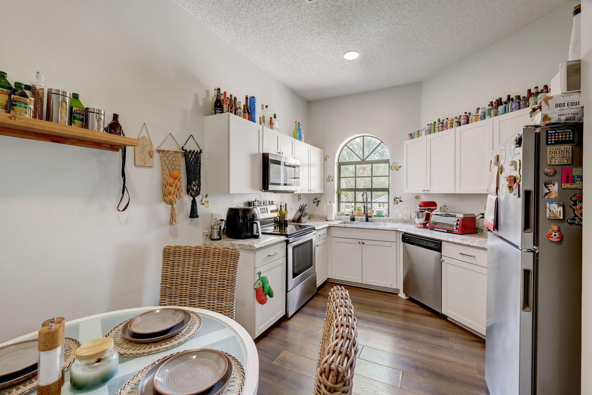 Kitchen with white cabinetry, stainless appliances, and an arched window above the sink.