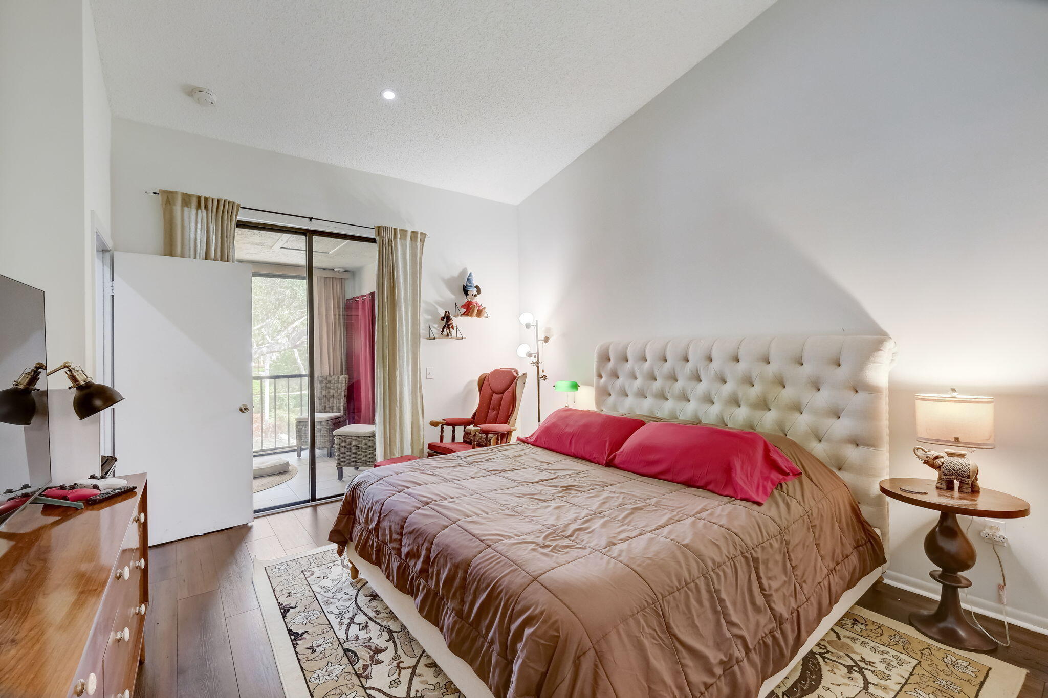 Bedroom with a vaulted ceiling, tufted headboard, red pillows, and sliding glass doors to a balcony.