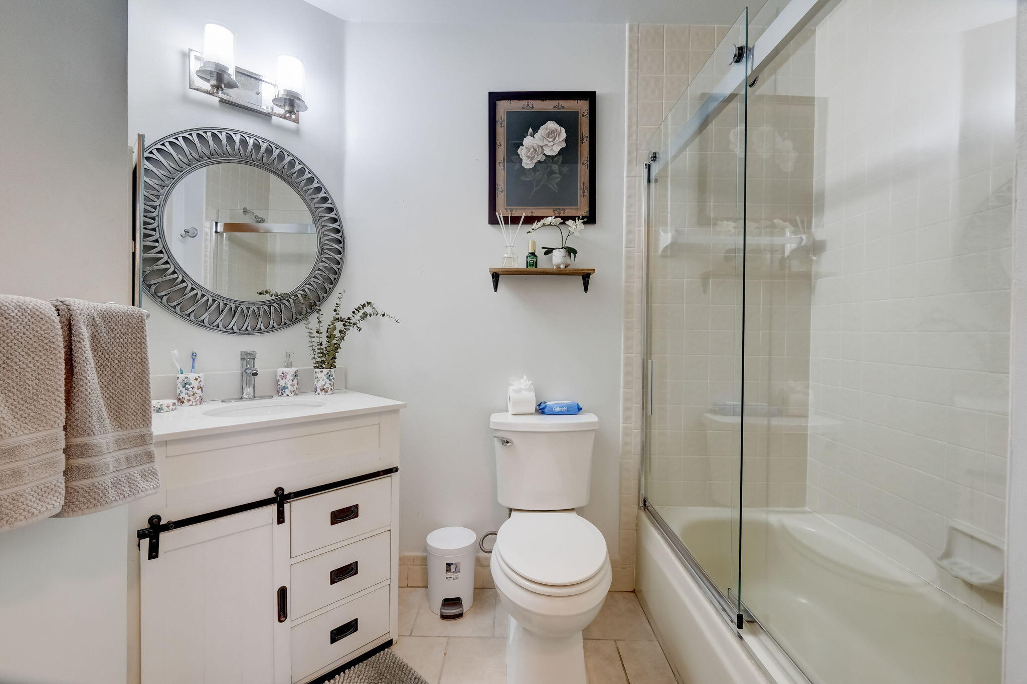 Bathroom with a white vanity, round mirror, and glass-enclosed tub and shower.