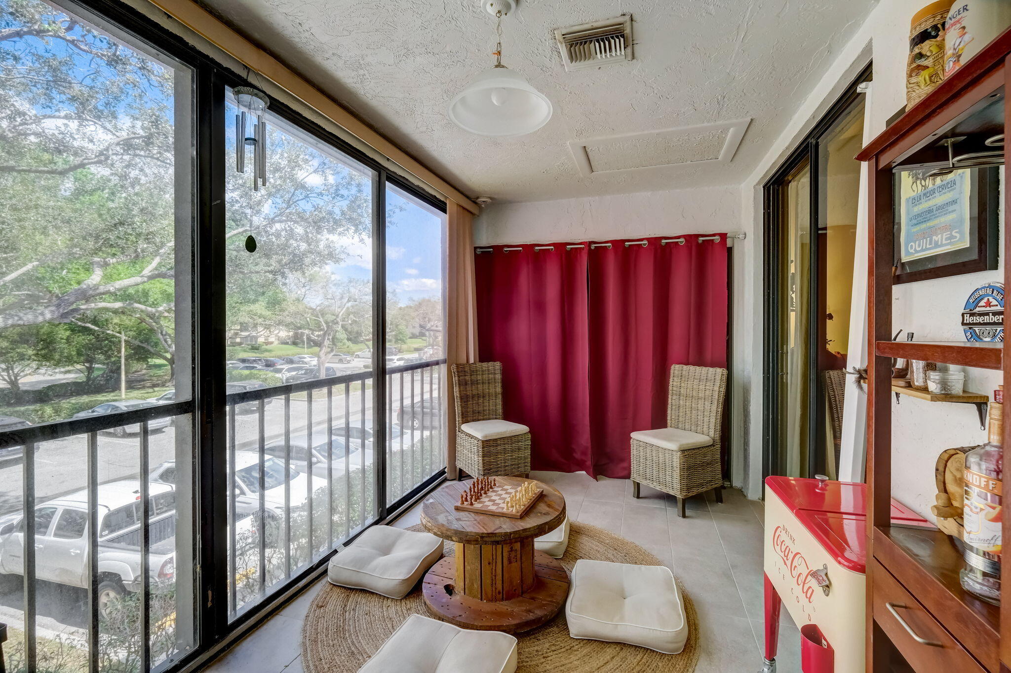 Enclosed sunroom with red curtains, wicker chairs, and a round table holding a chessboard.