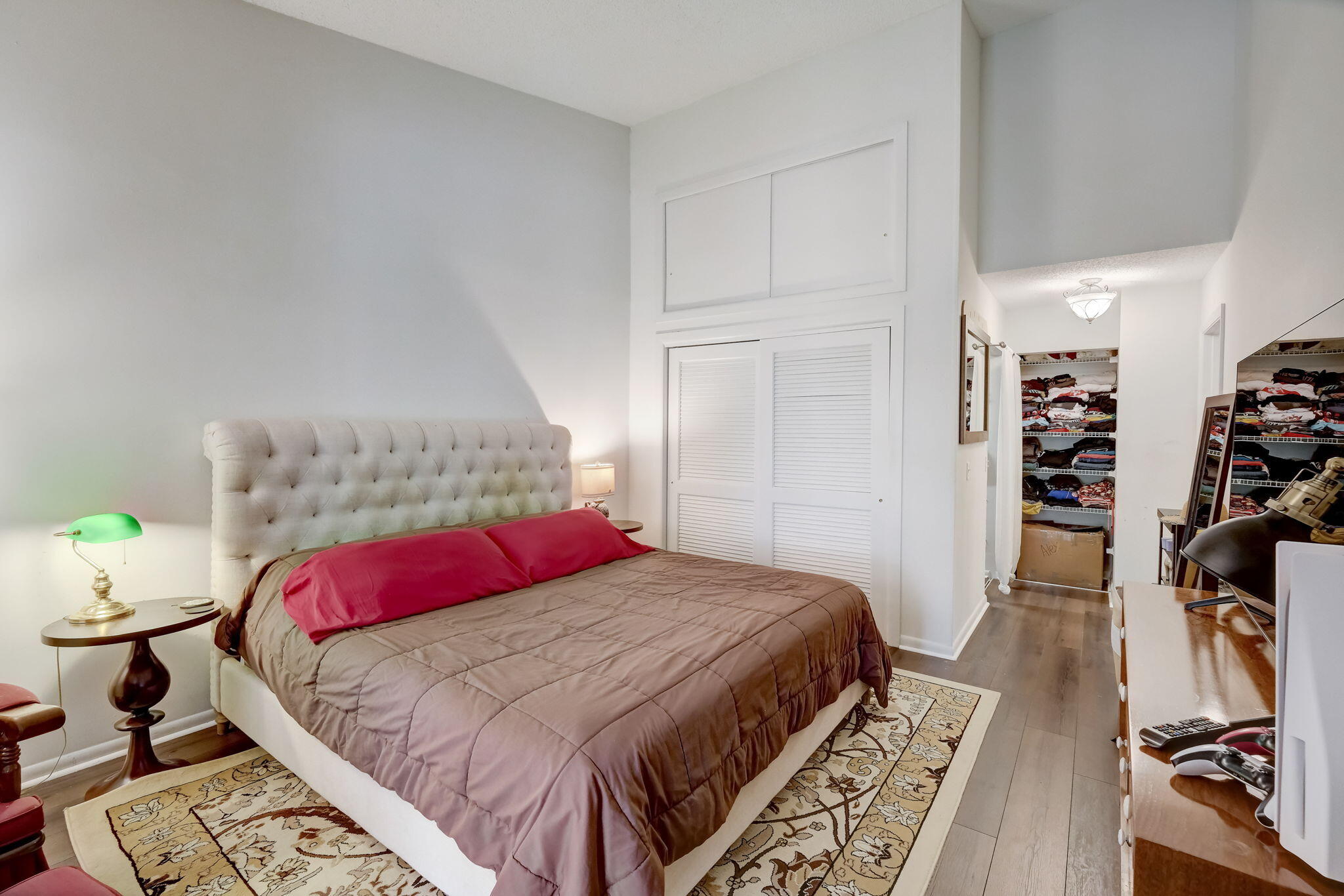 Furnished bedroom with a tufted headboard, pink pillows, patterned rug, and open linen closets.