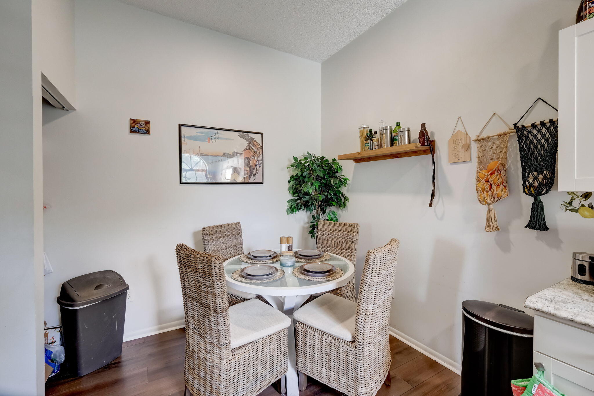 Dining nook with a round set table, woven wicker chairs, and a leafy potted plant.