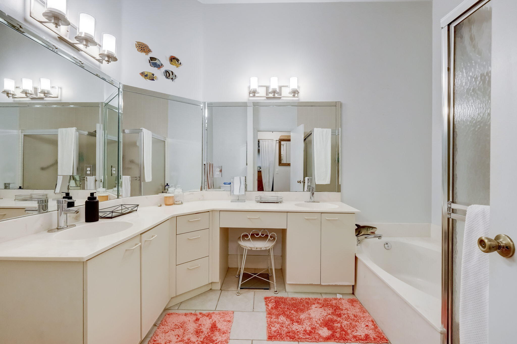 Bathroom with a long mirrored vanity, built-in makeup seat, bathtub, and coral rugs.