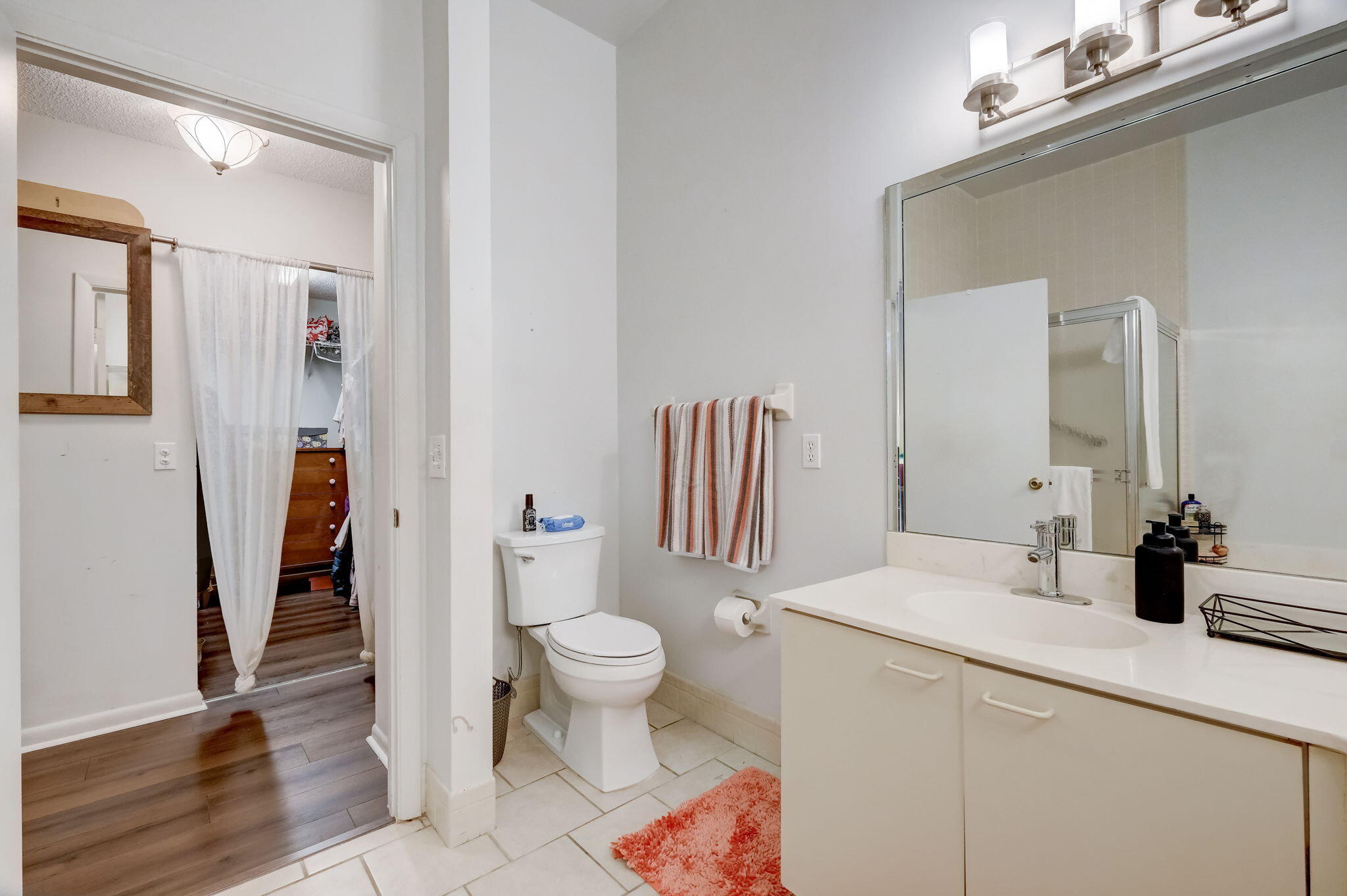 Bathroom with white vanity and large mirror, toilet, and doorway to a walk-in closet.