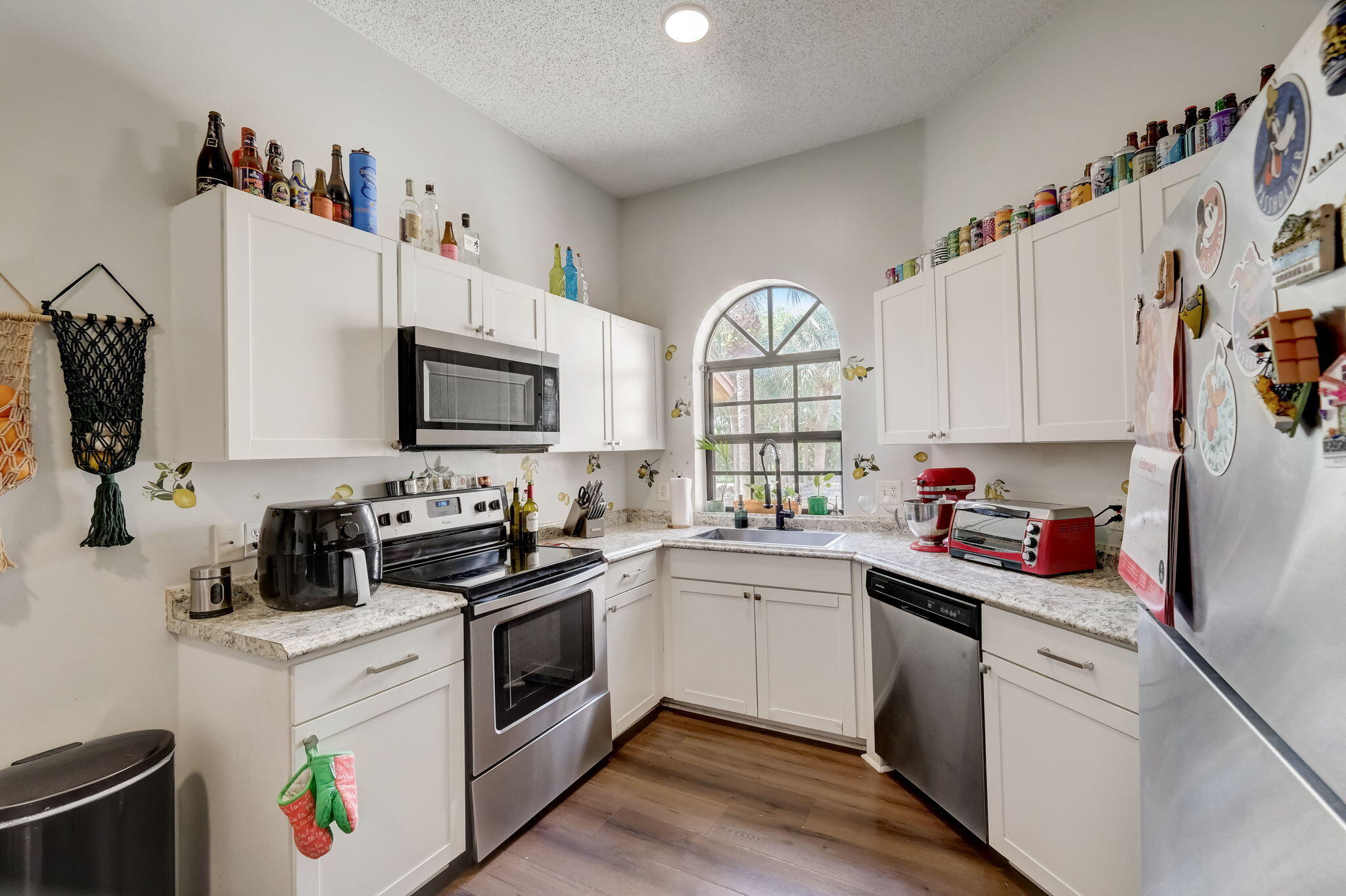 Kitchen with white cabinetry, stainless appliances, granite counters, and an arched window above the sink.